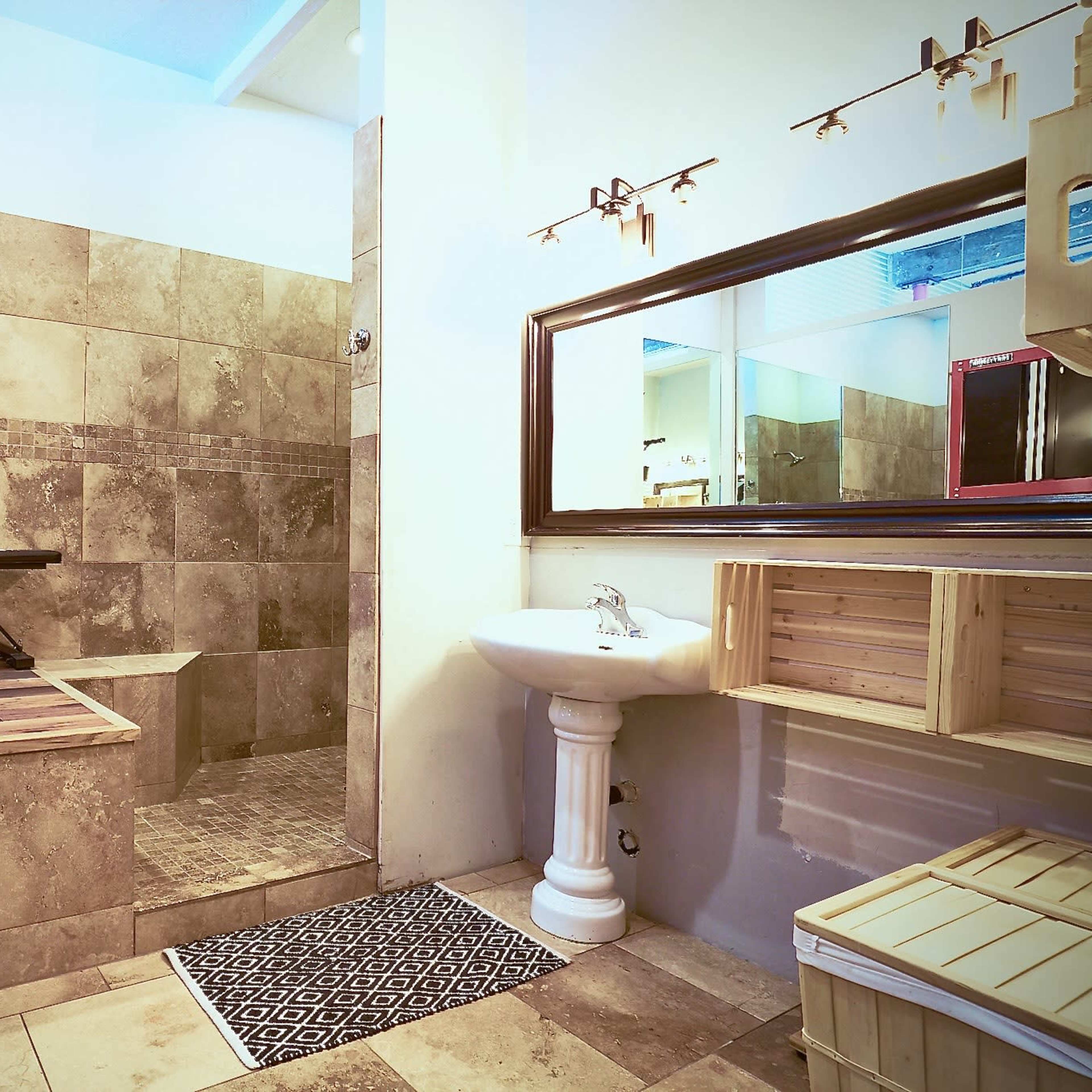 The bathroom features a large walk-in shower, a wooden bath platform with a blue exercise ball, and a single sink with a wooden storage unit.