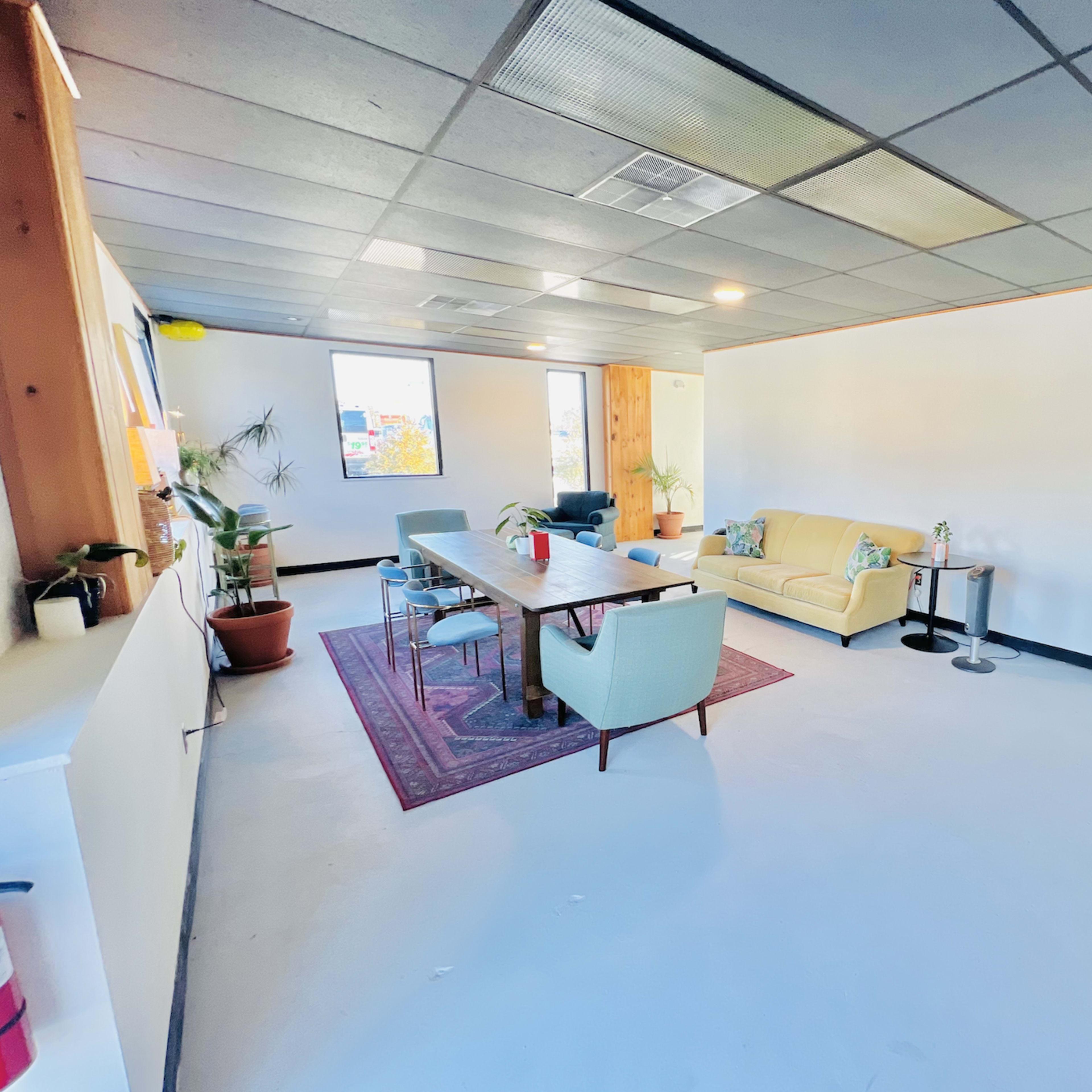 A spacious, minimalist lounge area with a long table, various seating options, and large windows.