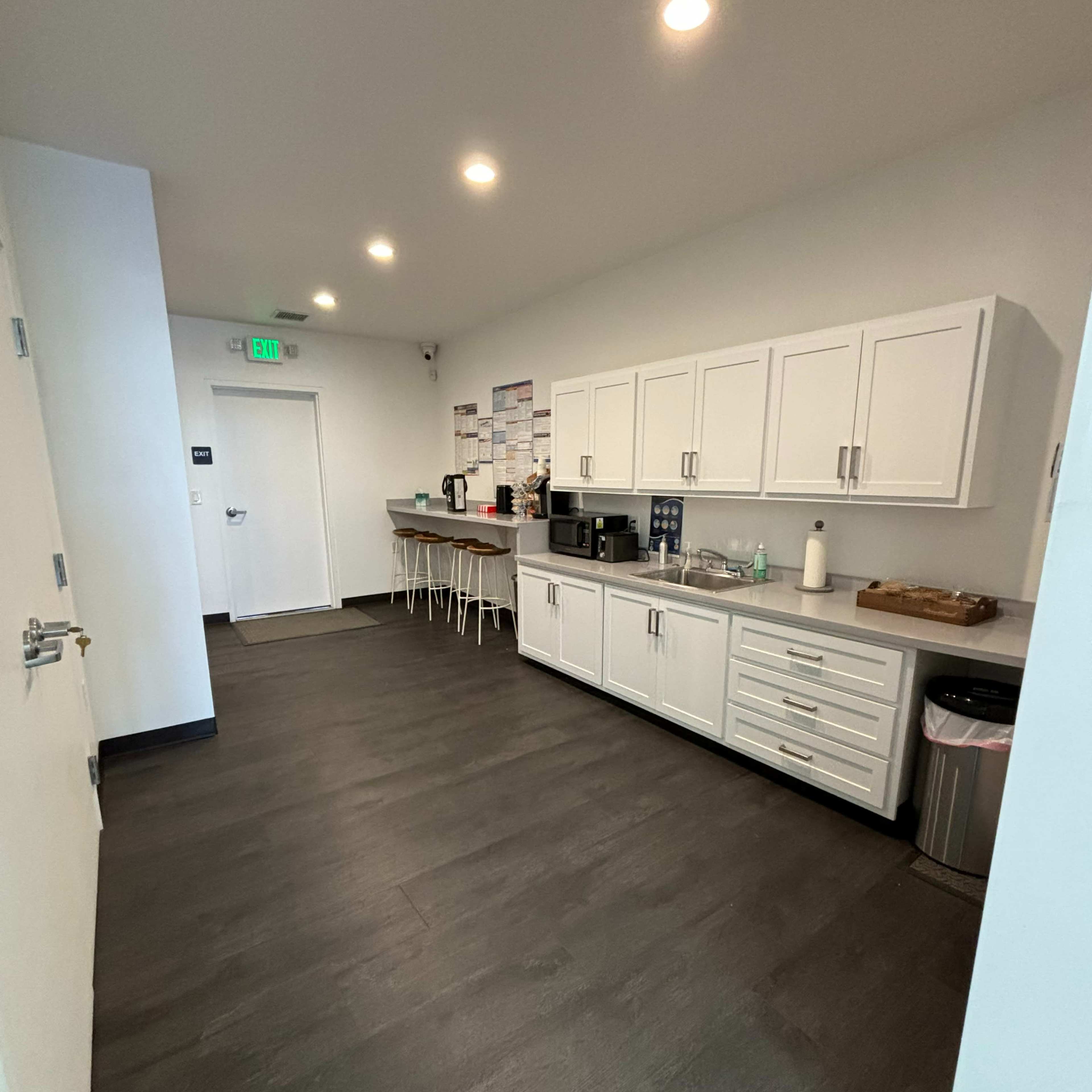 A modern kitchen area with white cabinetry, a countertop with appliances, and a clean floor.
