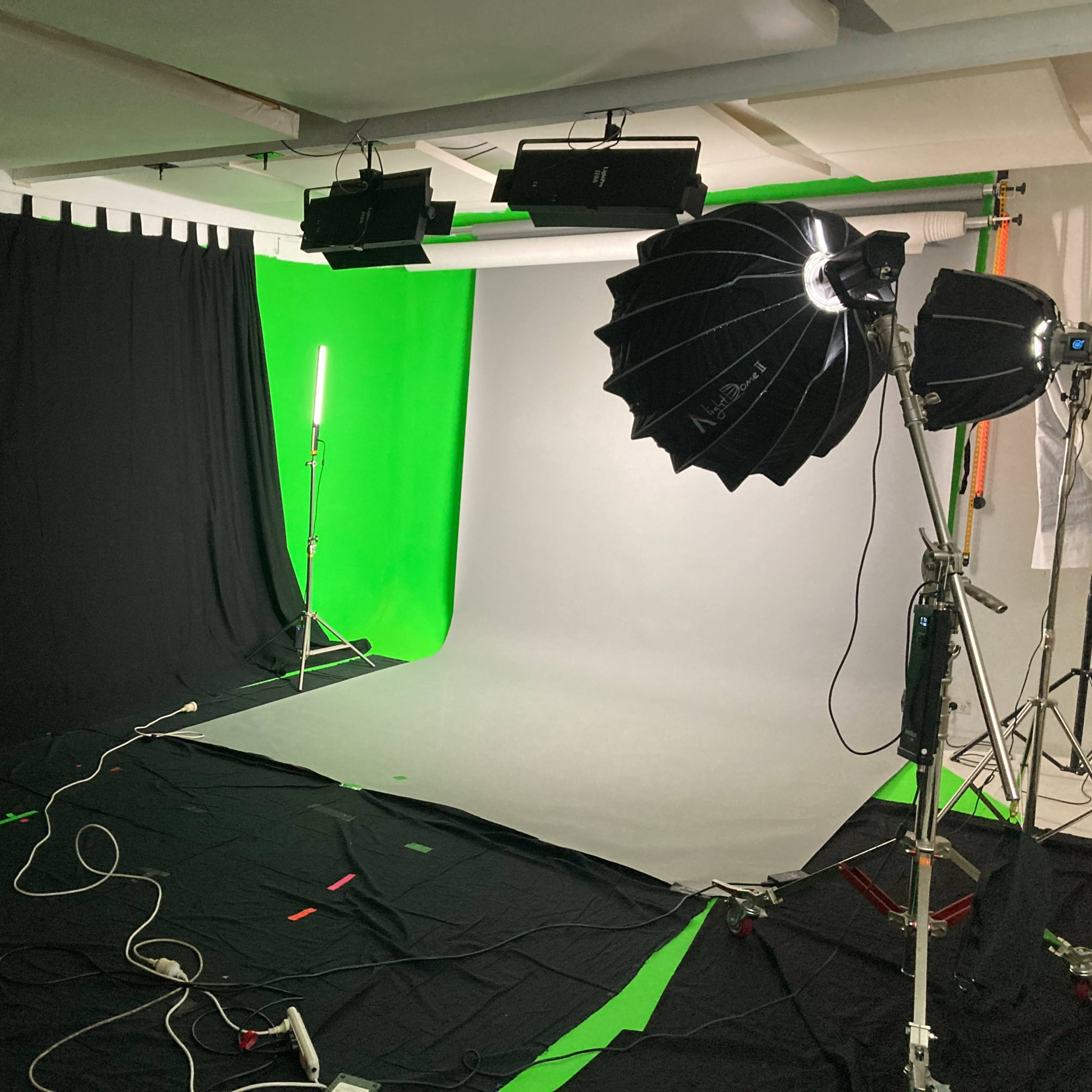 A photography studio setup with a green screen, a gray backdrop, and various lighting equipment arranged on the floor.