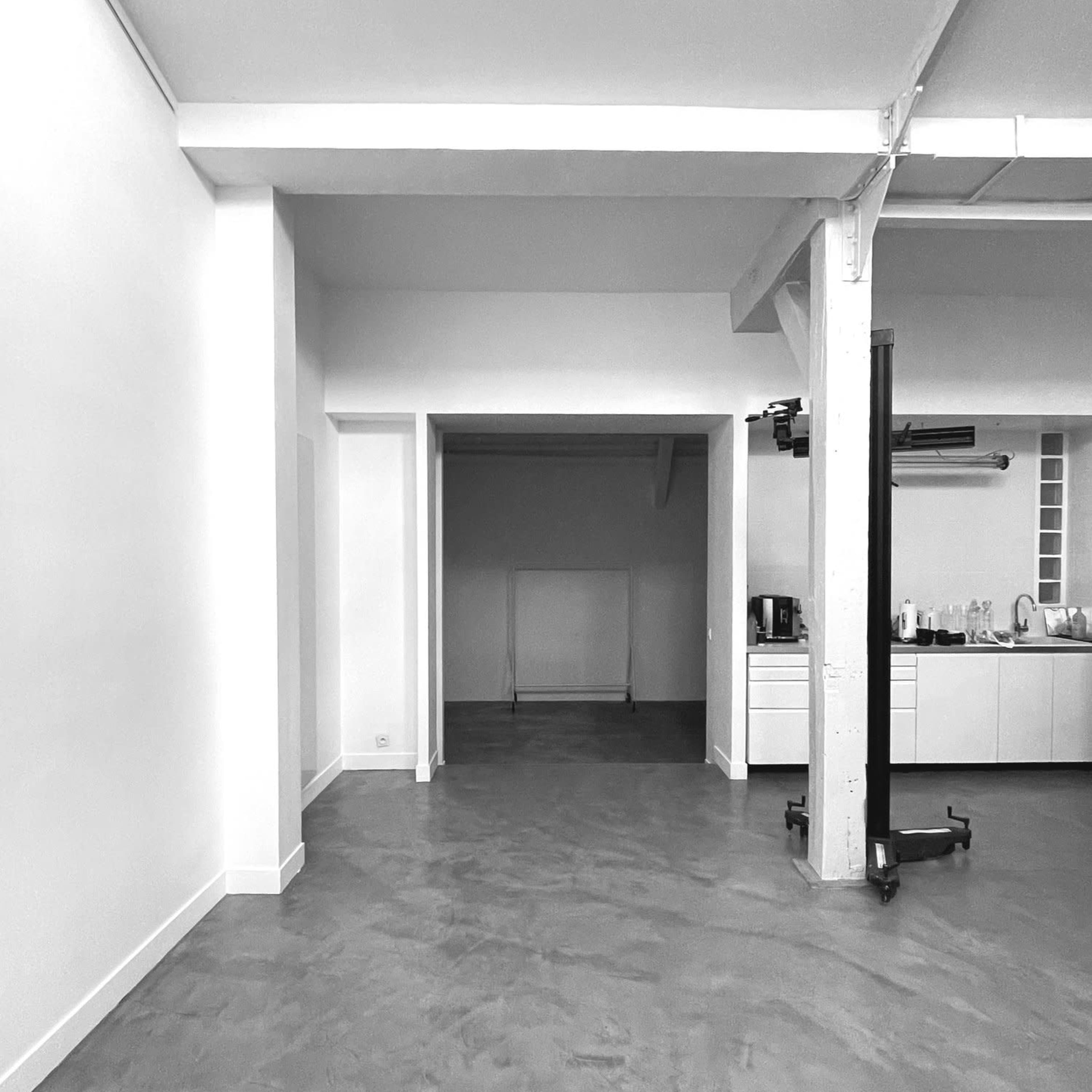 A spacious, empty room with concrete flooring and white walls, featuring an open doorway leading to another area.