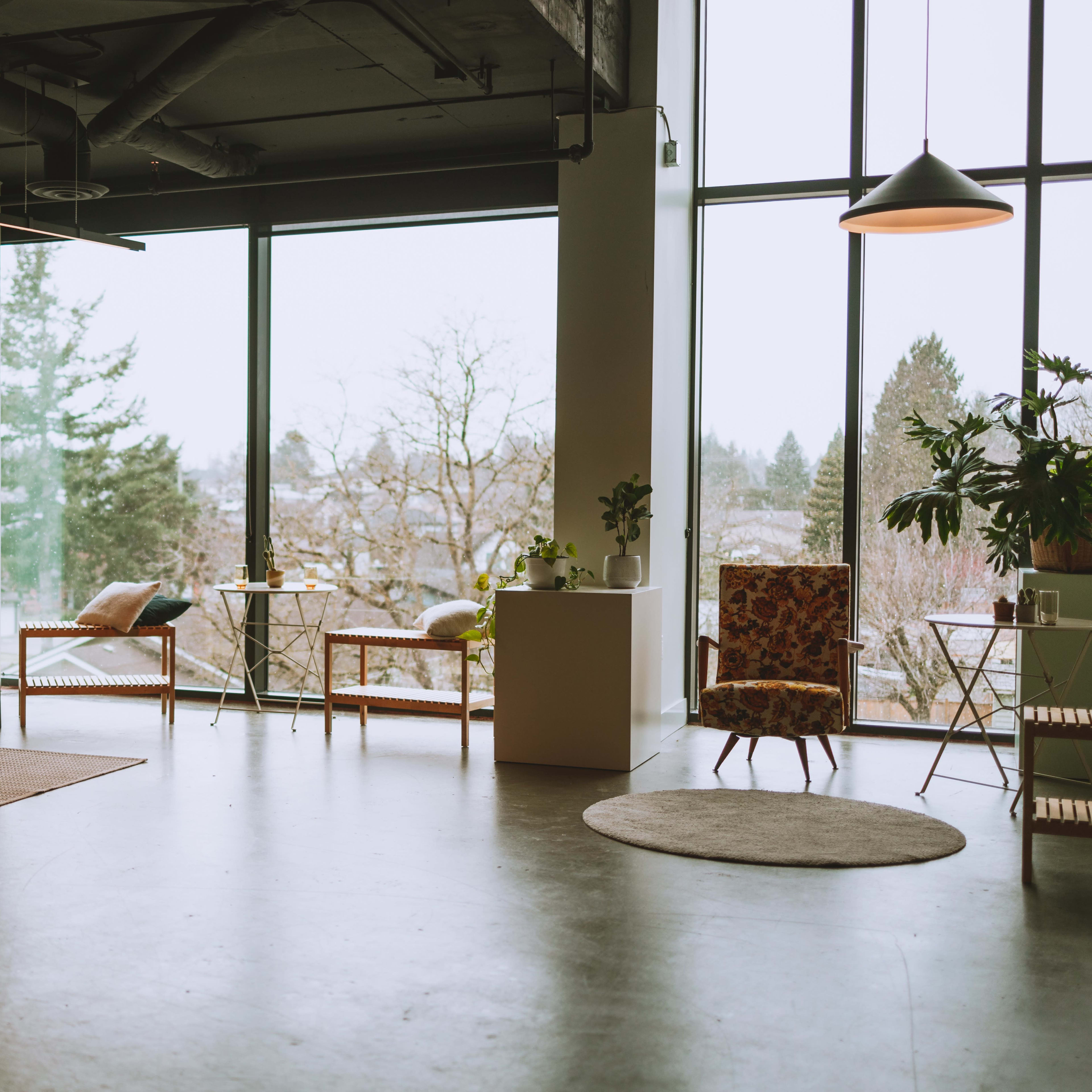 A spacious, modern living area featuring a brown sofa, a patterned chair, and large windows that overlook a tree-filled landscape.