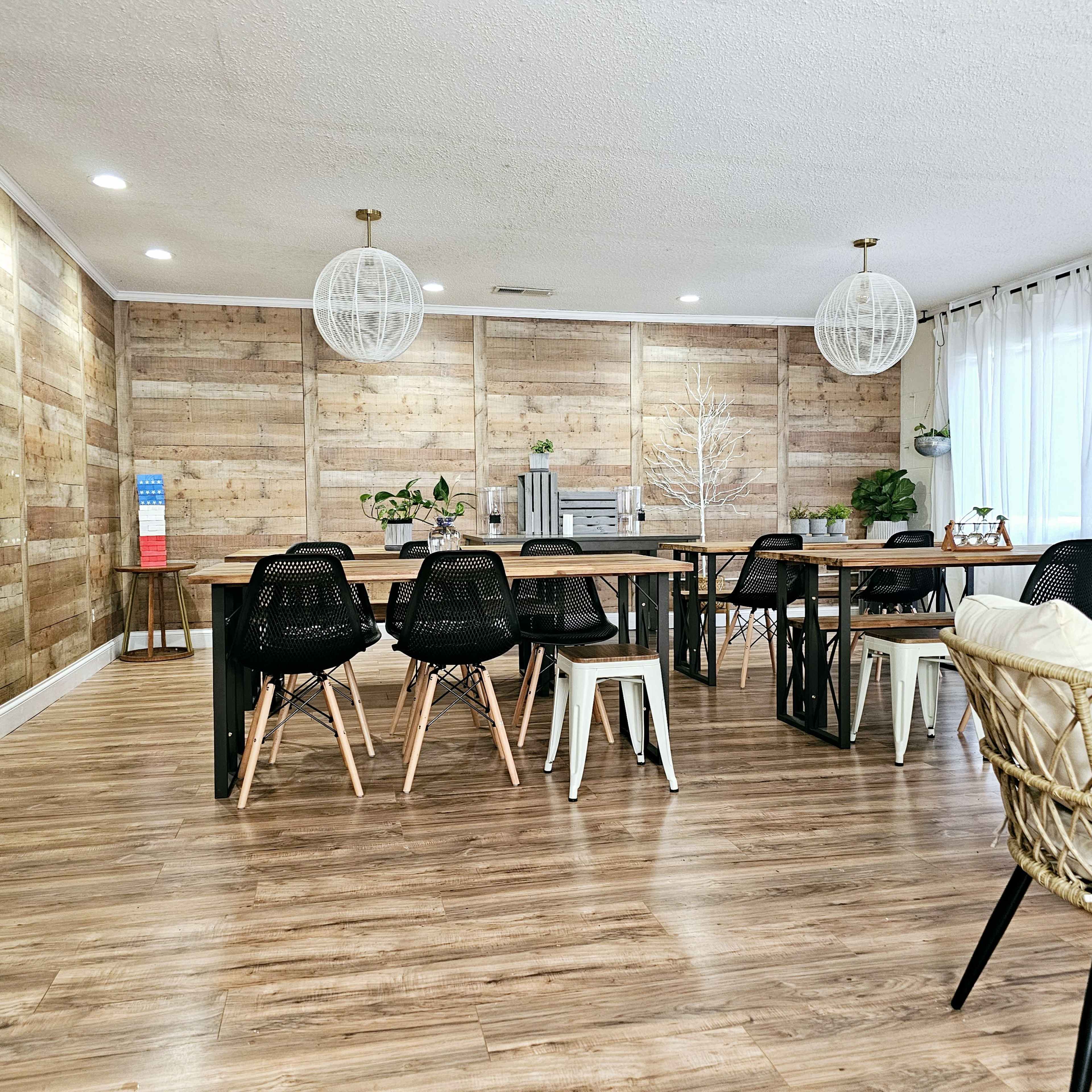 A spacious, open dining area featuring wooden walls, several tables with chairs, and pendant lighting.