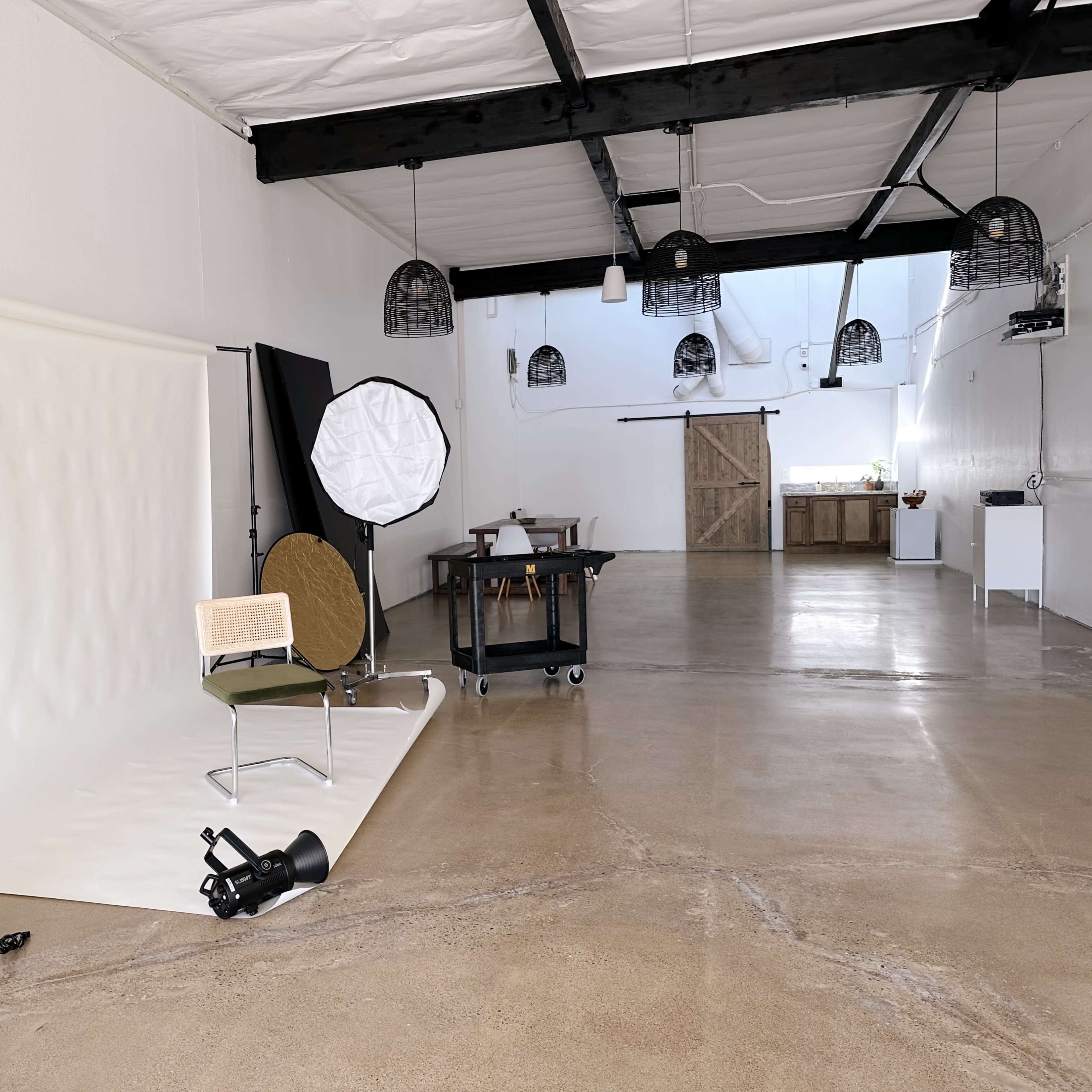 A spacious, minimally furnished studio with a photography setup, including a backdrop, lighting equipment, and a chair.