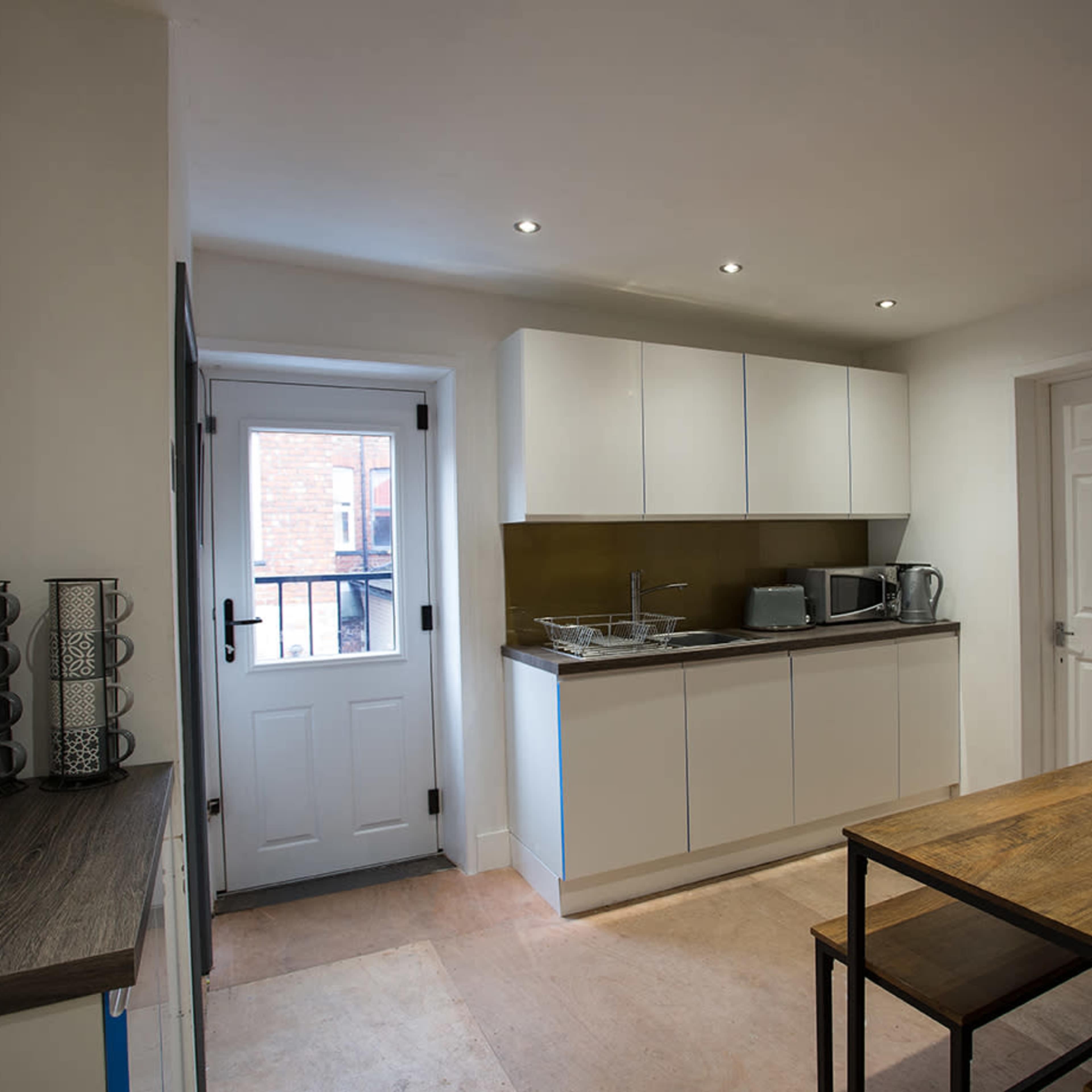 A modern kitchen features white cabinetry, a stainless steel countertop, and a wooden dining table with magazines on it.