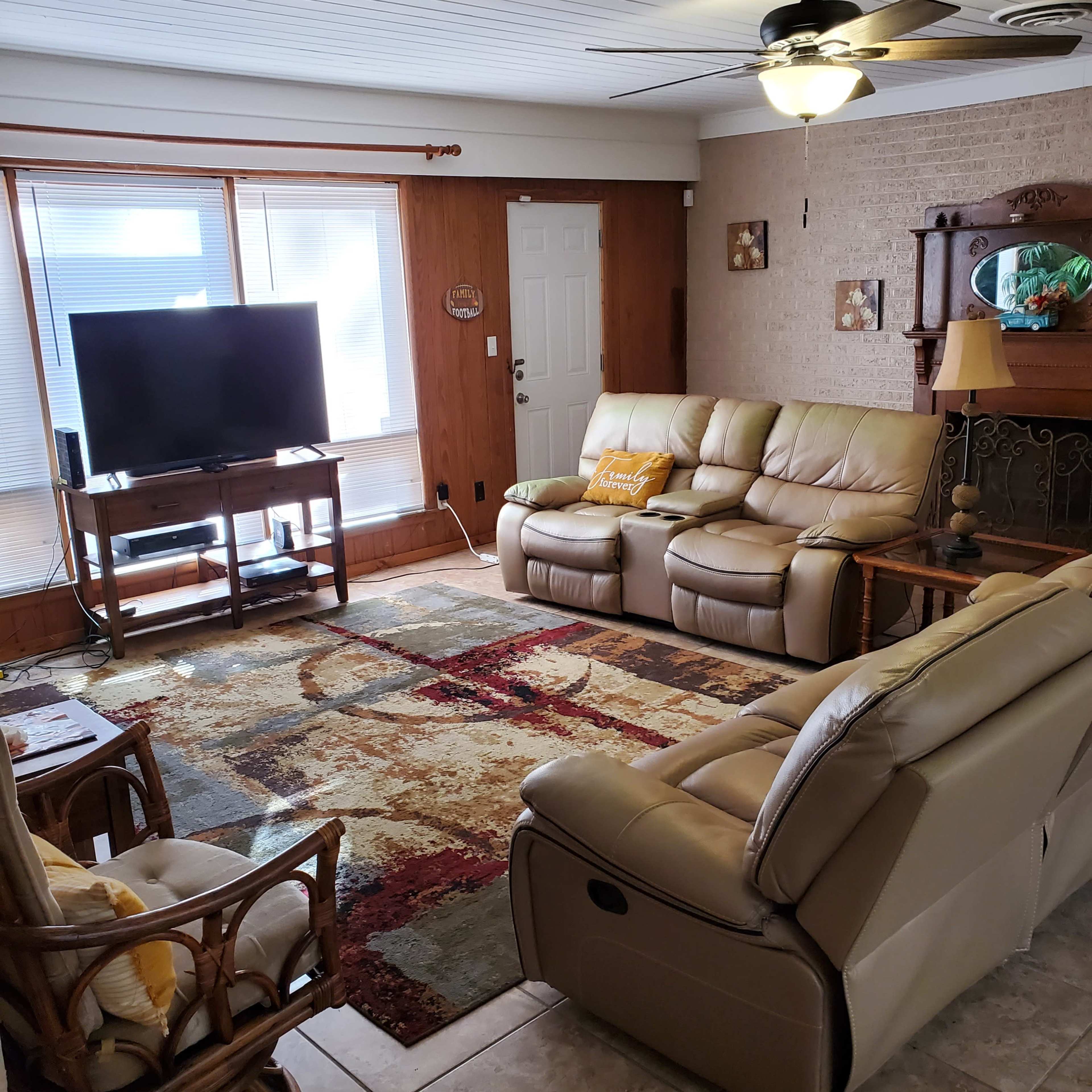 A living room with two leather sofas, a television, and a decorative area rug on tiled flooring.