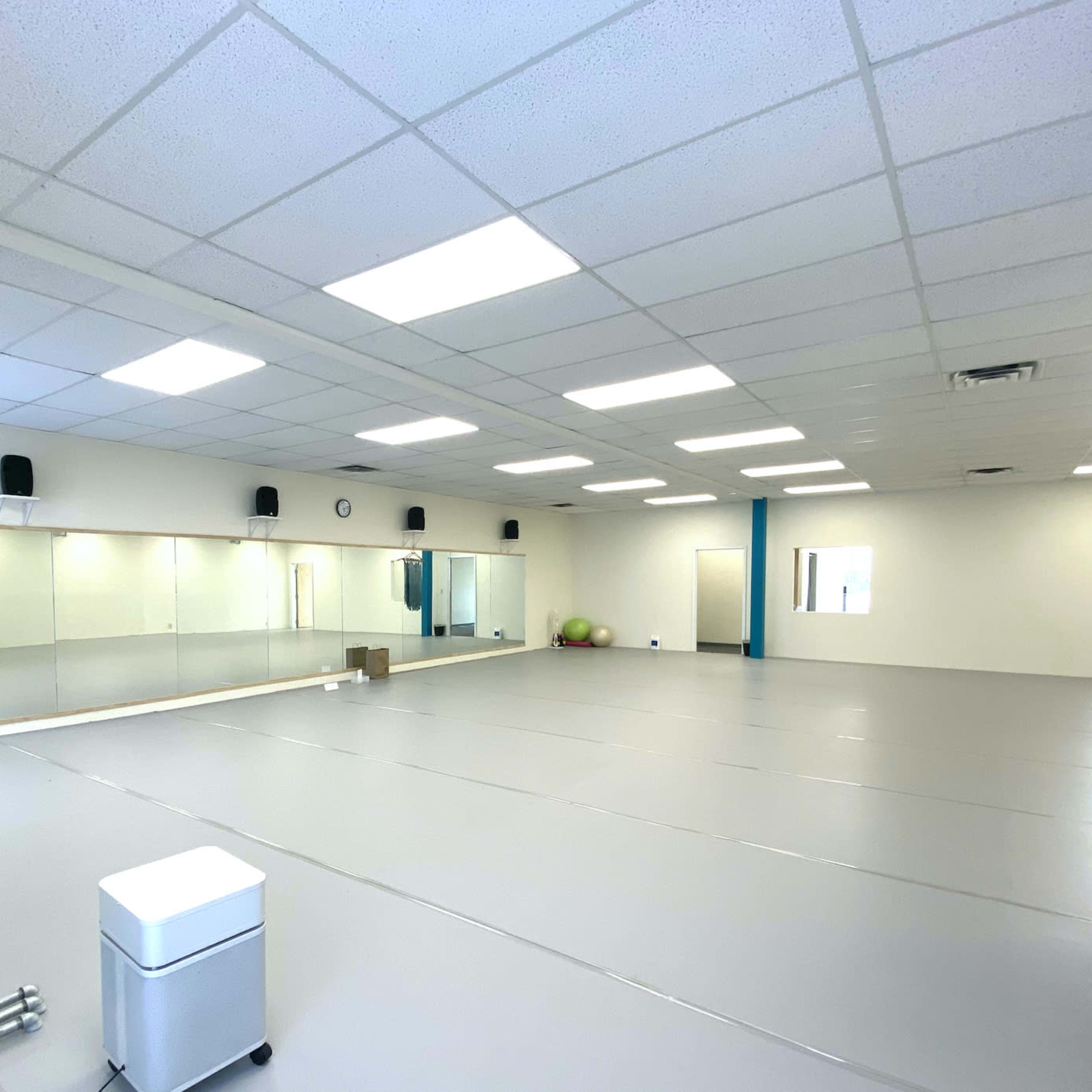 A spacious, empty room with mirrored walls, gray flooring, and minimal furnishings.