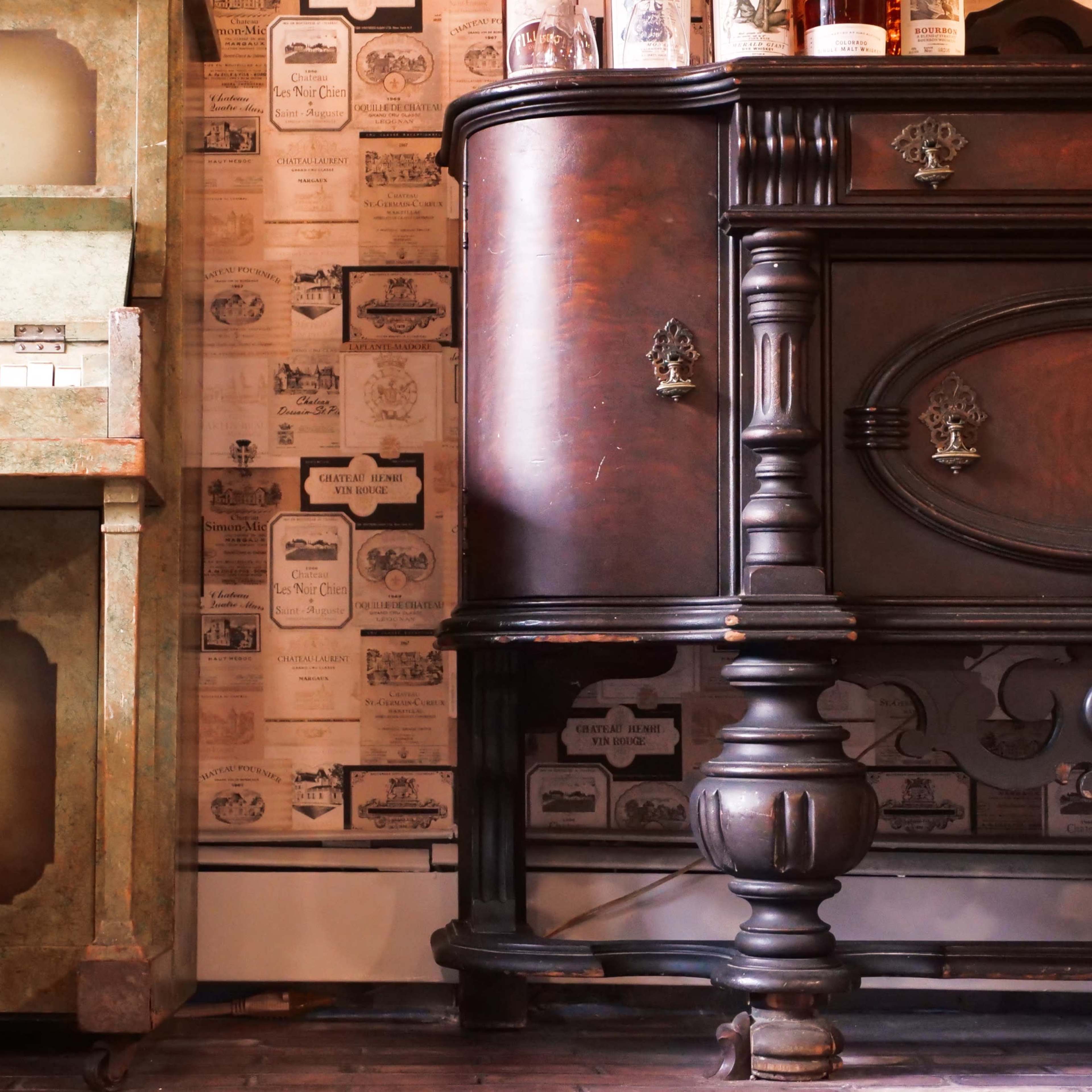 A green vintage piano next to an ornate dark wooden cabinet, both set against a wall covered with old advertisements.