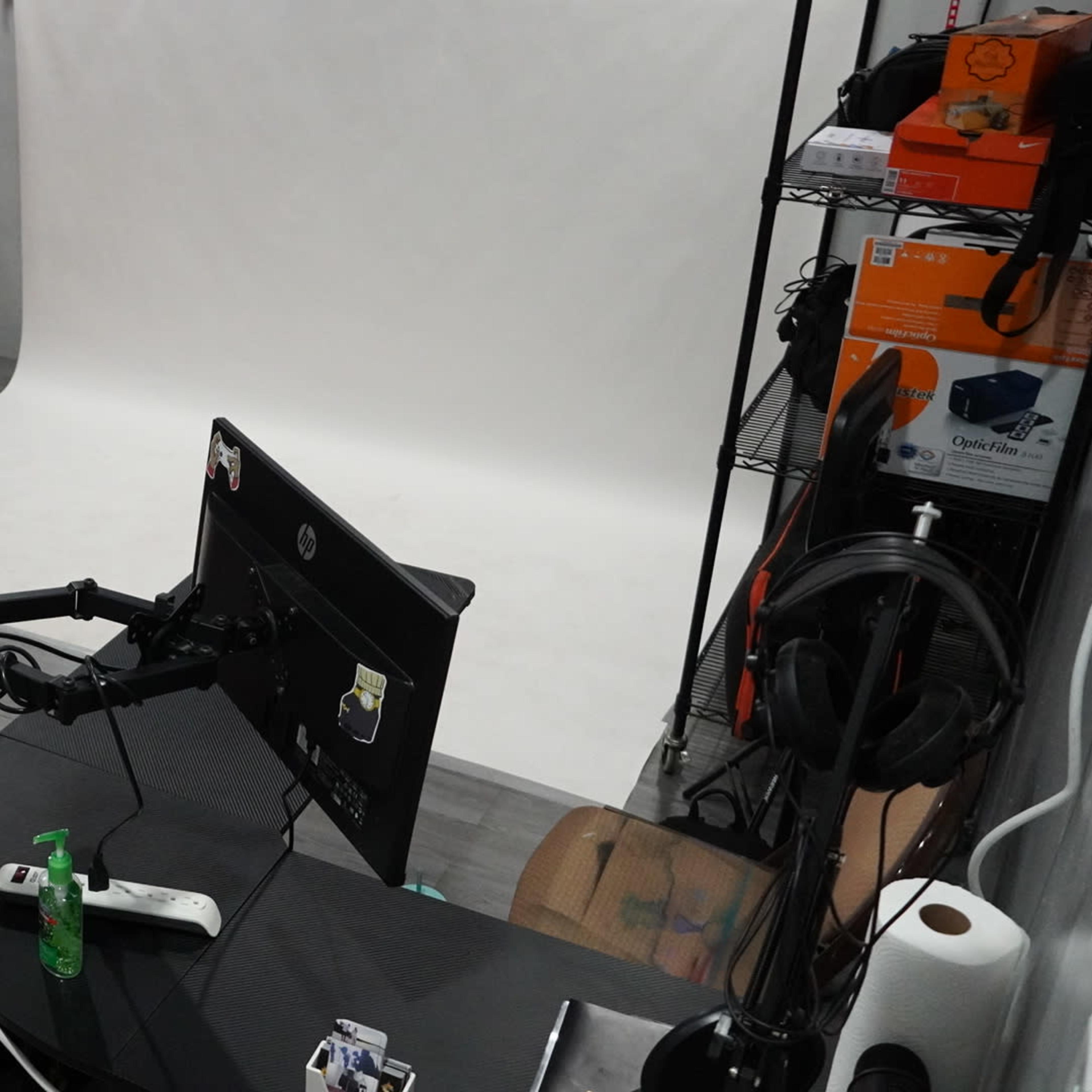 A modern creative workspace with a black desk, computer monitor, and a white backdrop for photography against a red-brick wall.