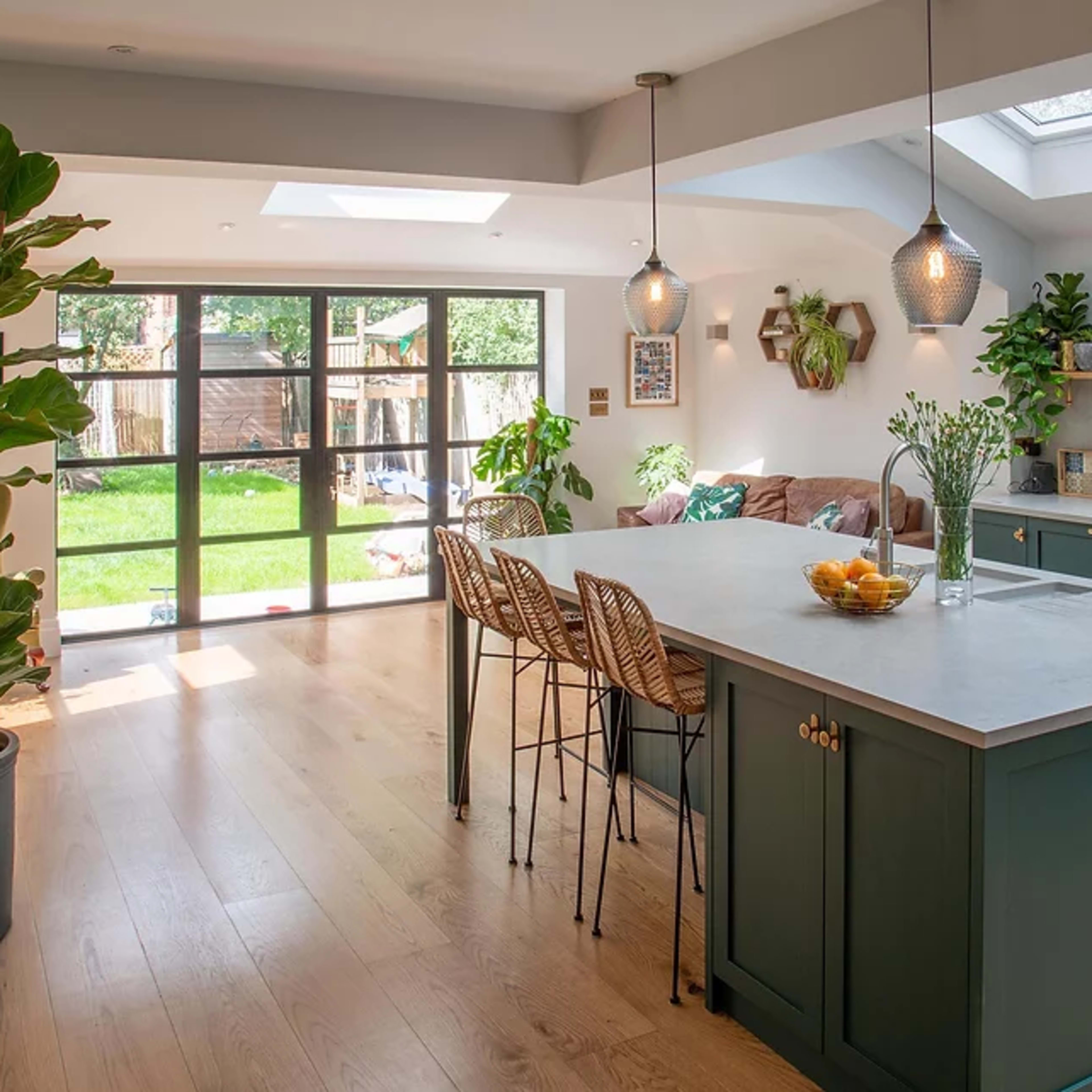 A modern kitchen features an island with bar stools, a sliding glass door opening to a backyard, and ample sunlight streaming through the skylights.