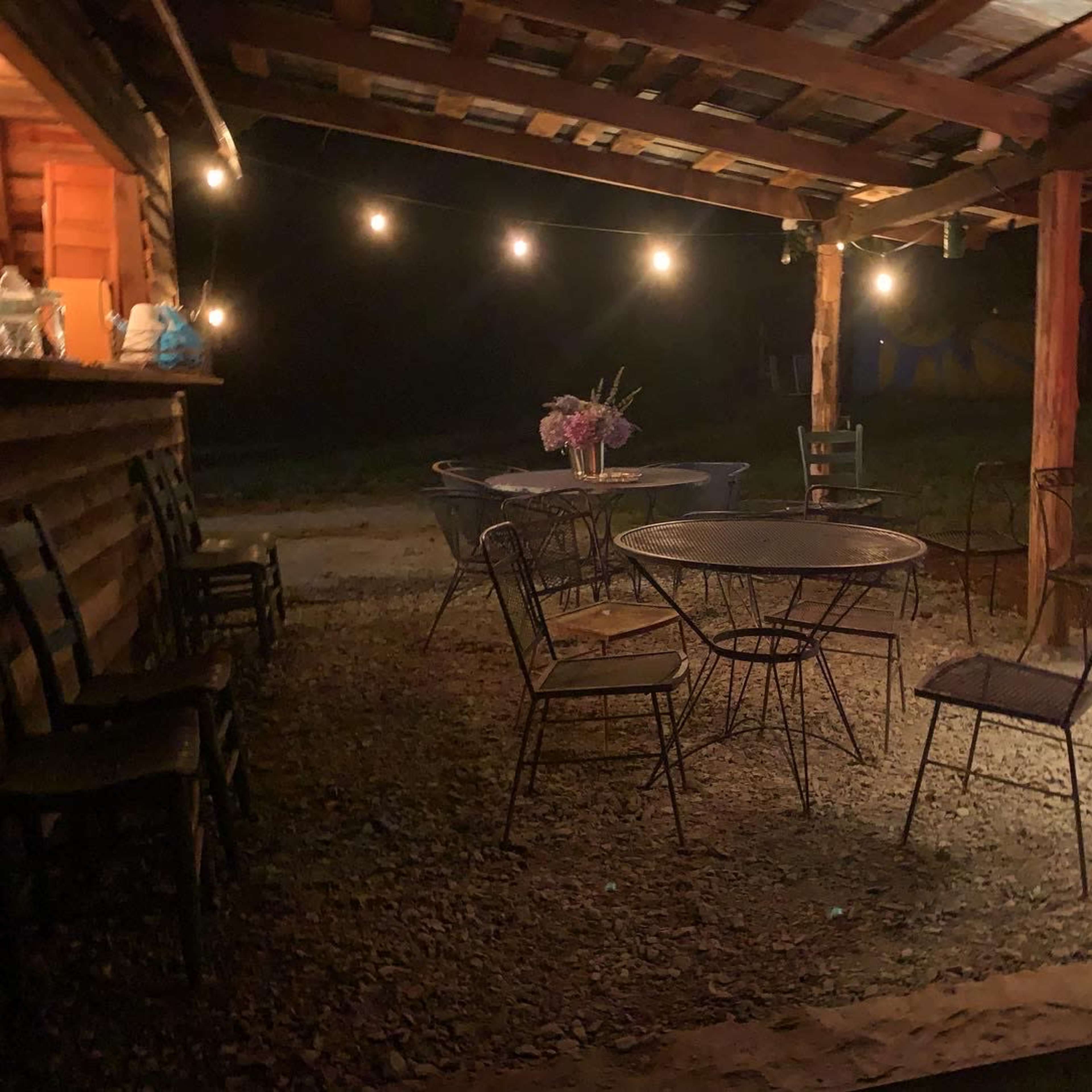 The scene shows an outdoor patio area with several chairs and tables illuminated by string lights and a hanging red lantern.