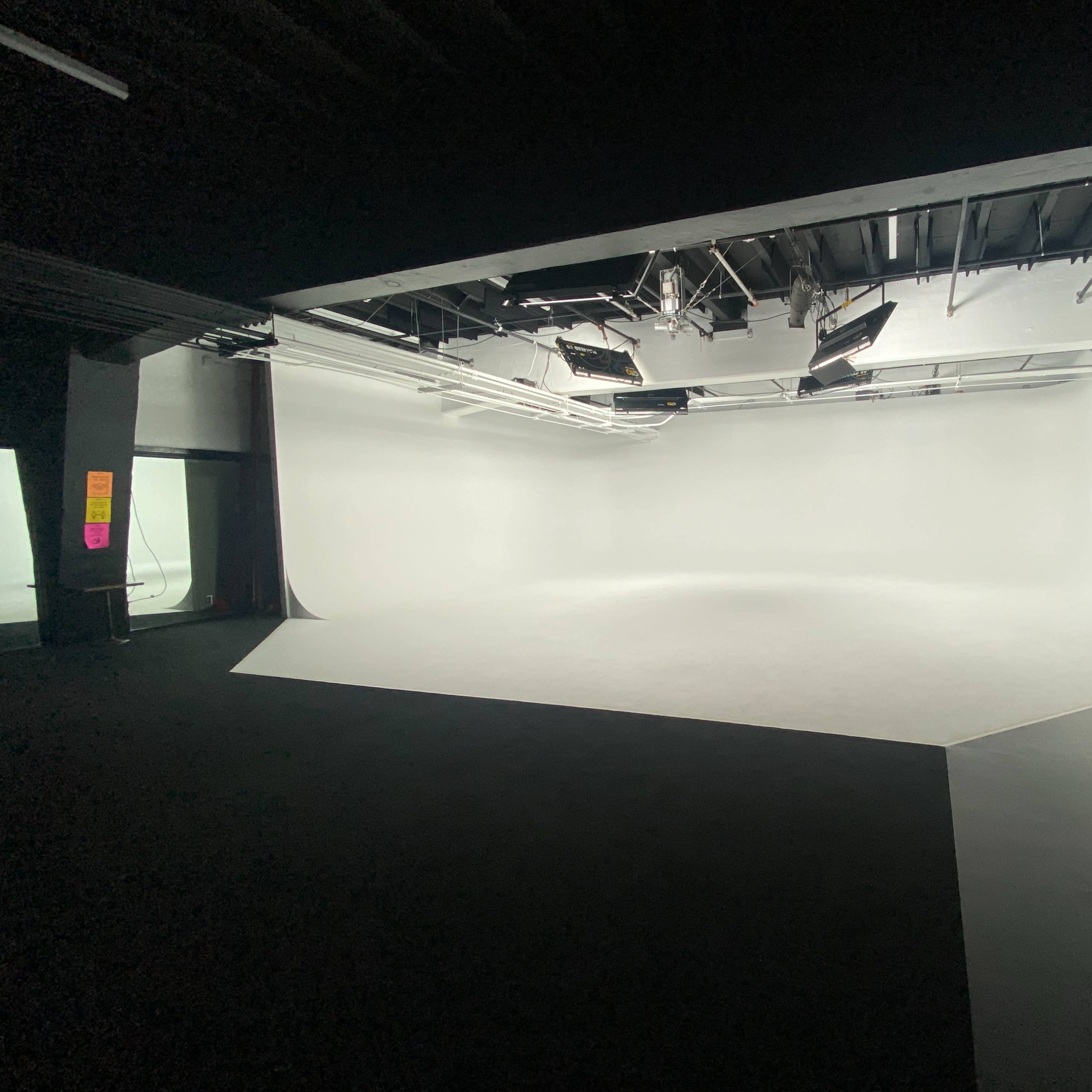 An empty photography studio with a seamless white backdrop and overhead lighting.