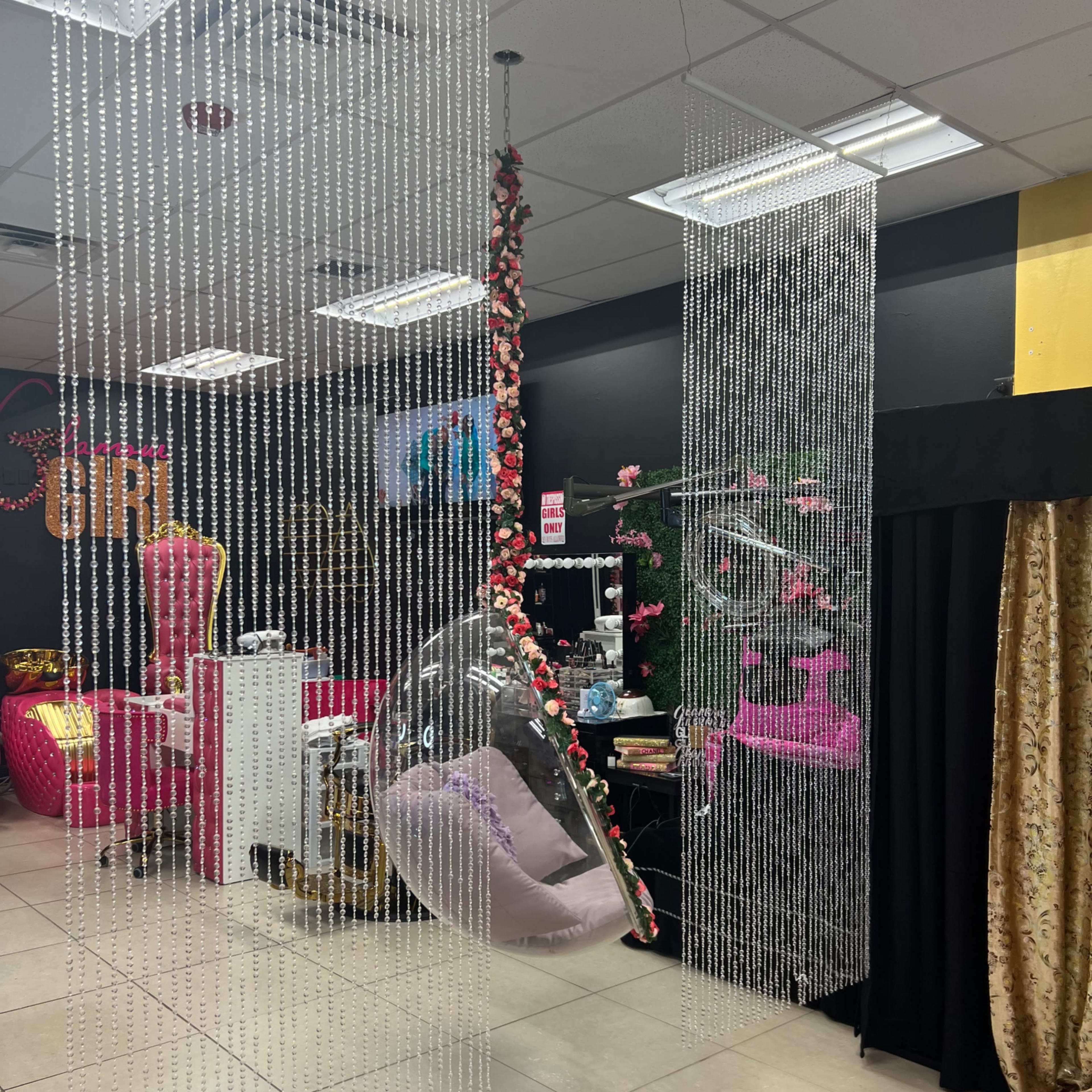 A salon interior decorated with hanging crystal bead curtains, a transparent hanging chair, and colorful furniture against a black wall.