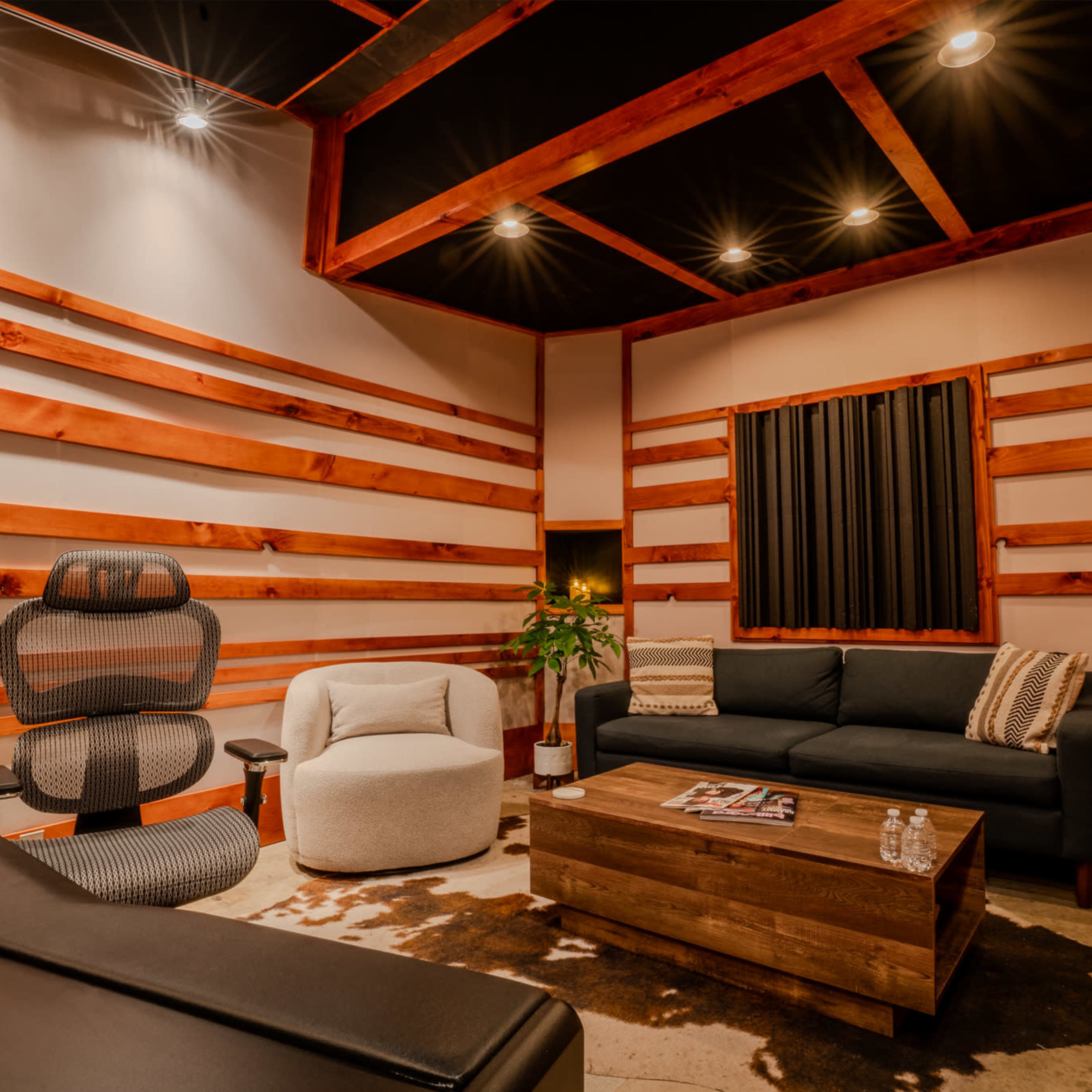 A modern interior space featuring a sectional couch, a lounge chair, a wooden coffee table, and wooden wall accents, all illuminated by recessed lighting.