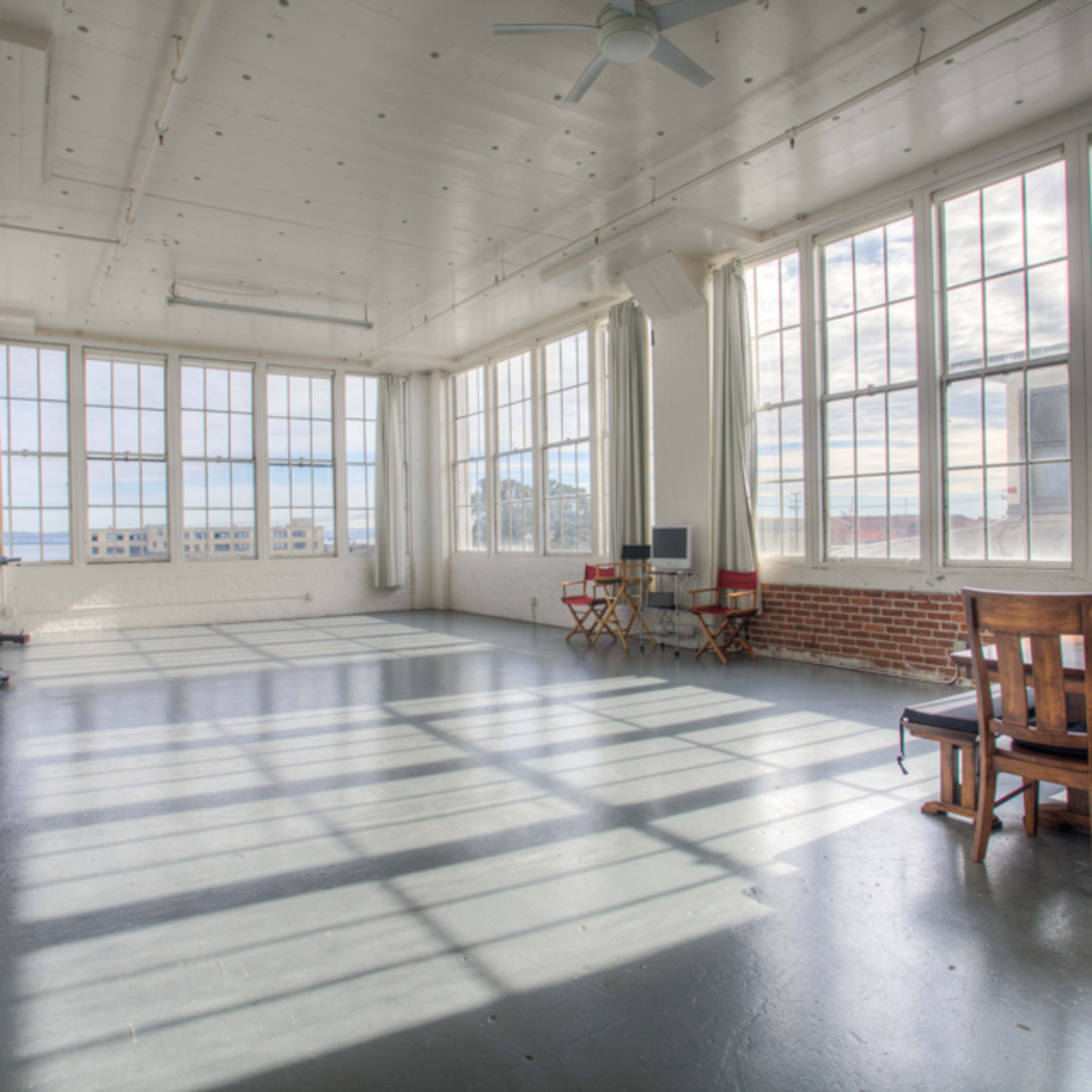 A spacious room with large windows, wooden furniture, and a dining table, illuminated by natural light.