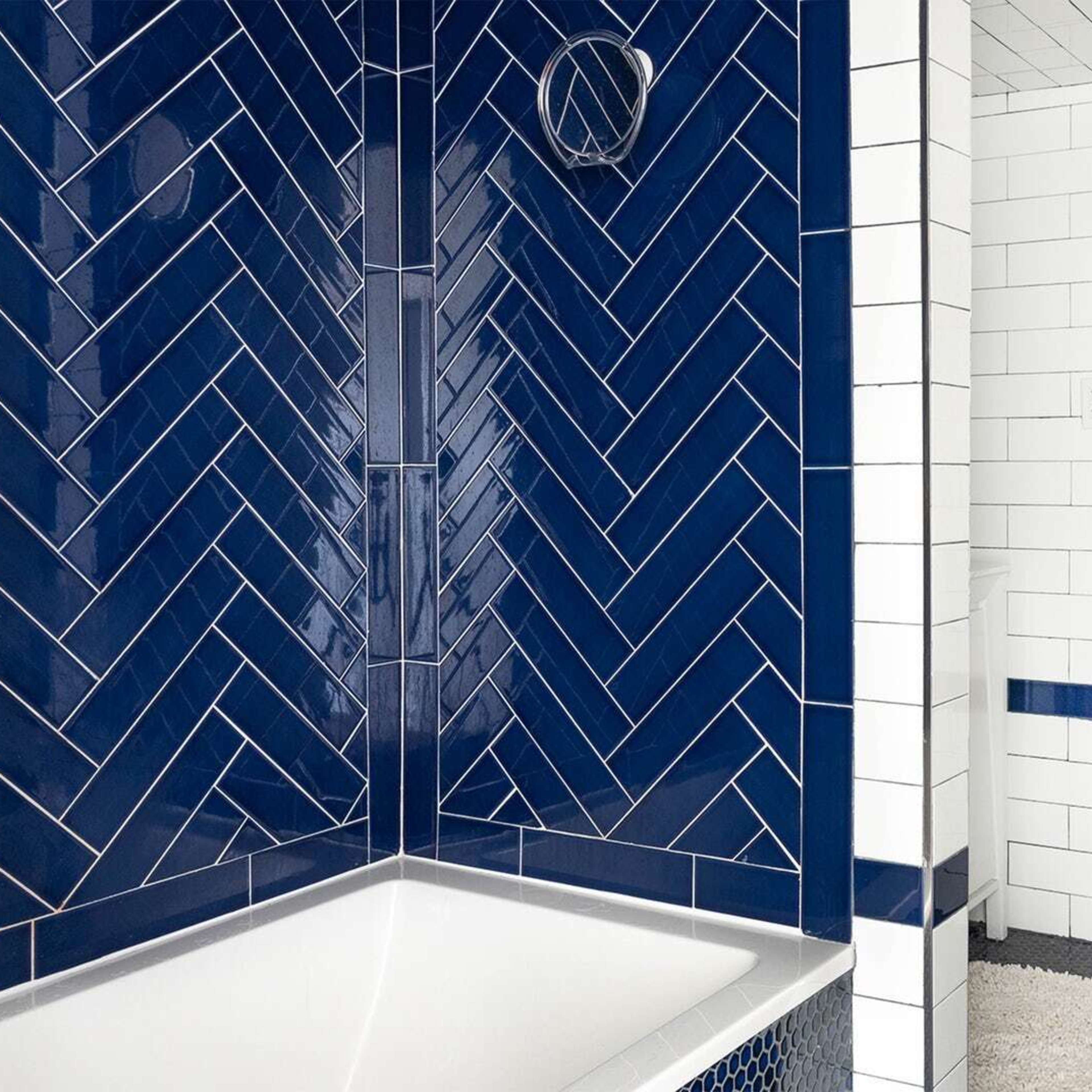 A bathroom with a white tiled wall and dark blue herringbone patterned tiles surrounding a bathtub.