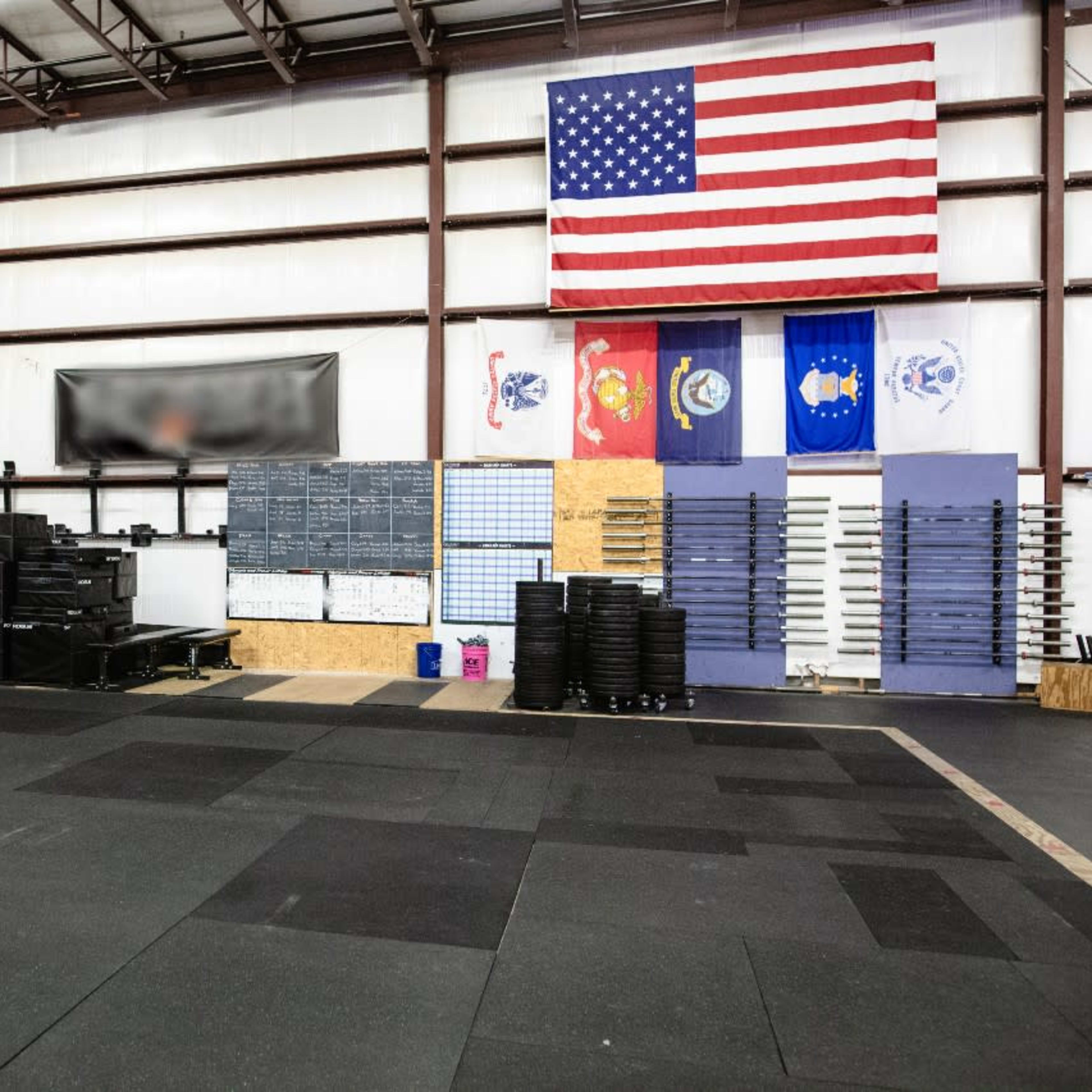 The interior of a gym featuring workout equipment, a rubber floor, and various flags hanging on the wall.