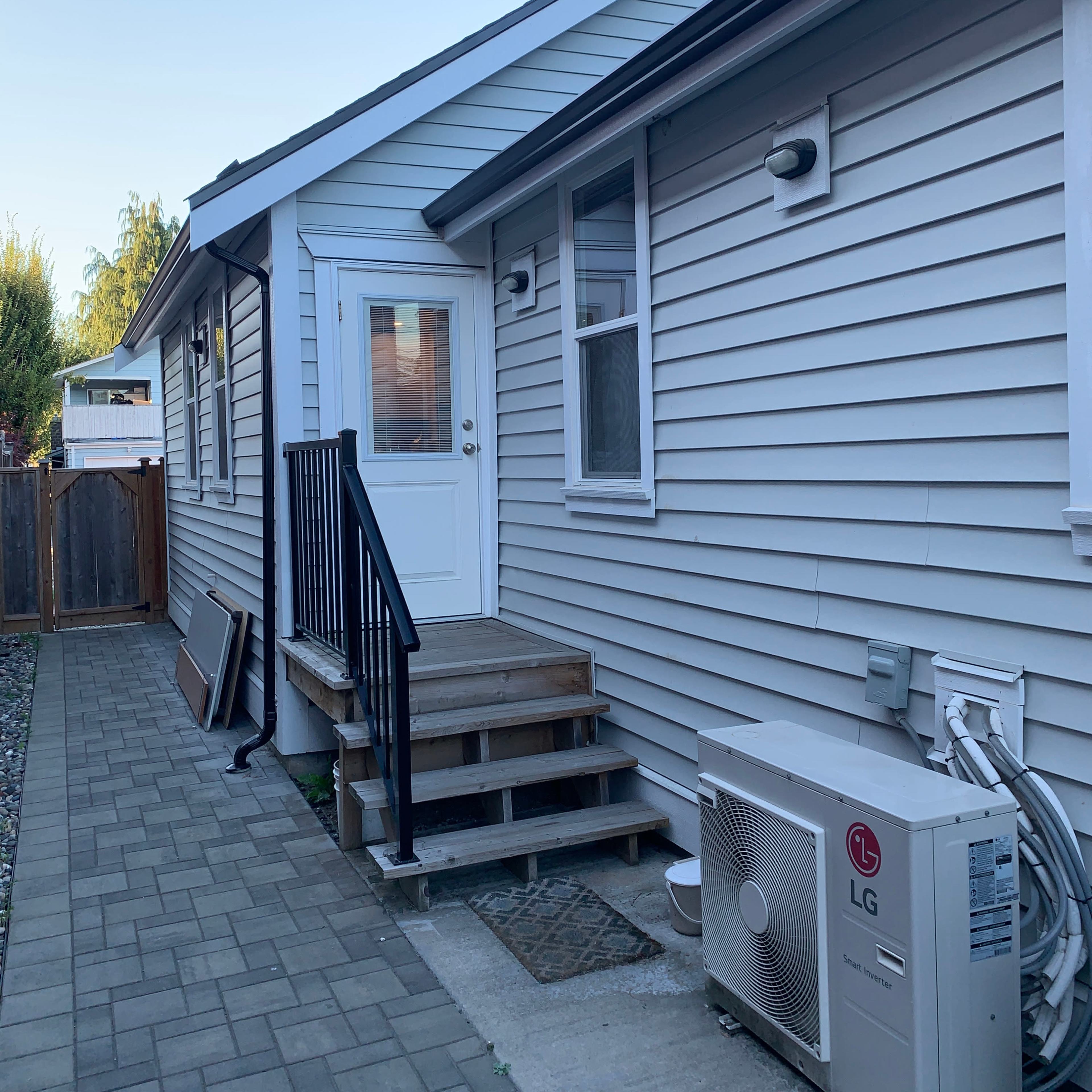 A gray house features a side entrance with stairs and an air conditioning unit beside it.