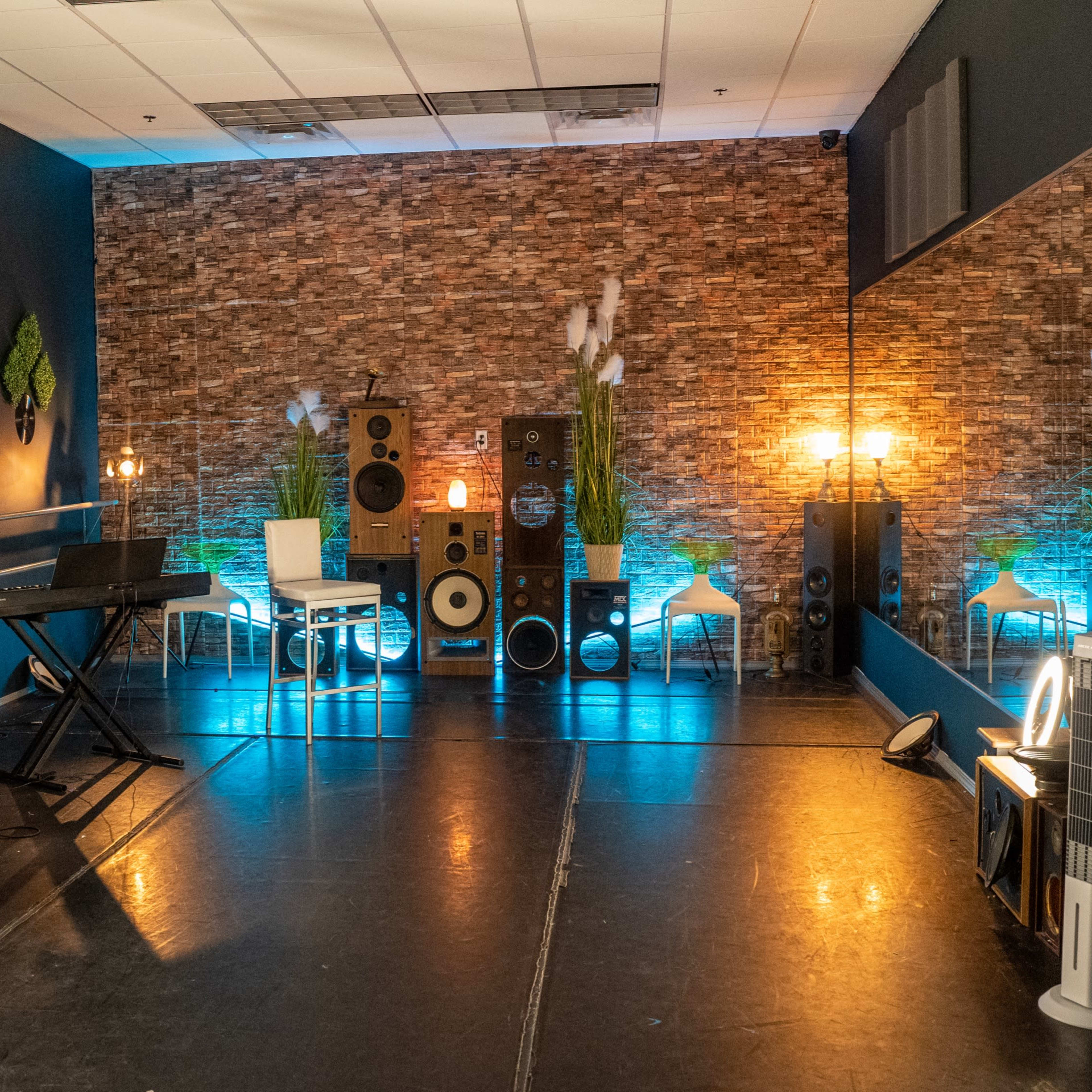 A music studio with speakers, a keyboard, an acoustic guitar, and seating arranged against a textured wall.