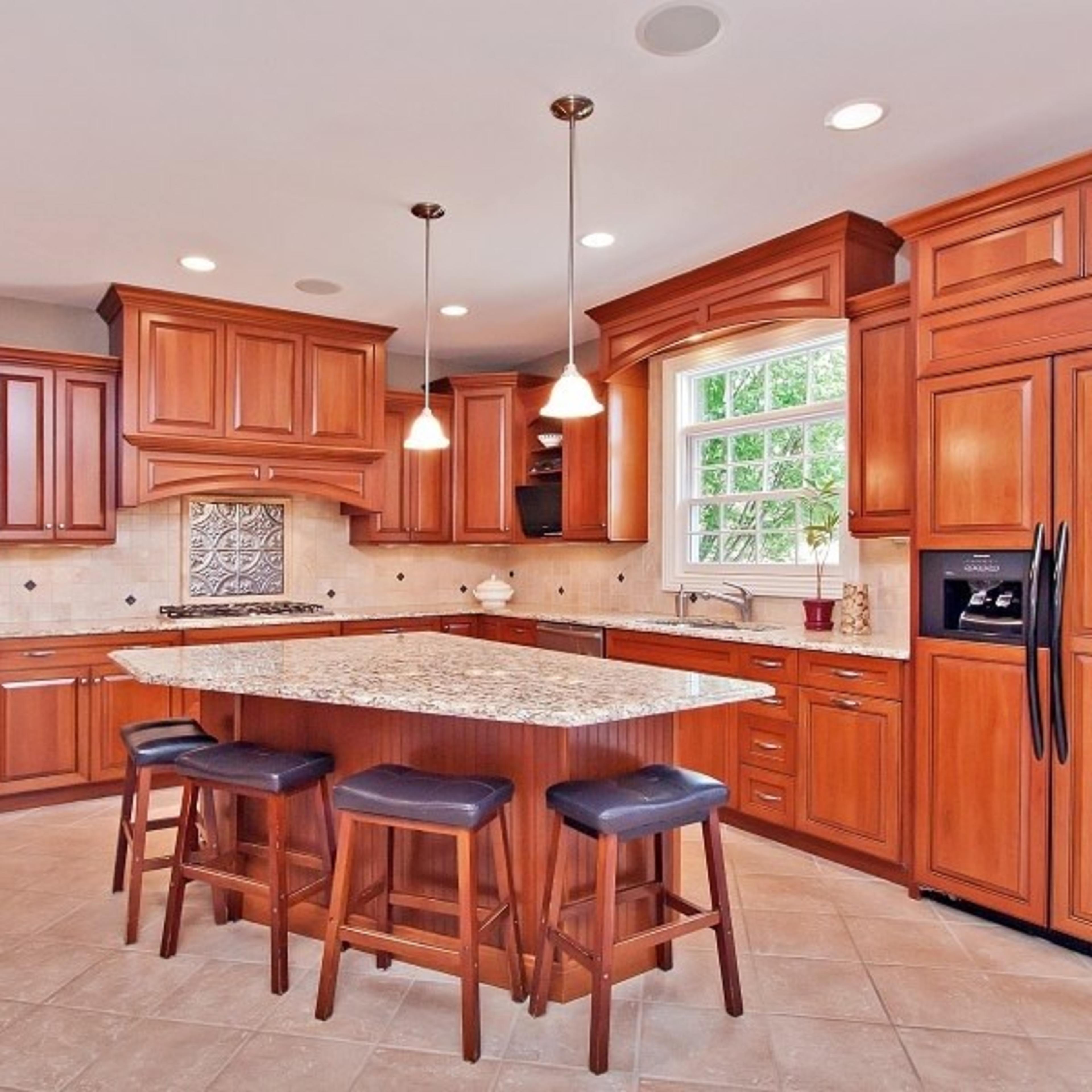 A modern kitchen with wooden cabinetry, a large island with a granite countertop, and pendant lighting above.