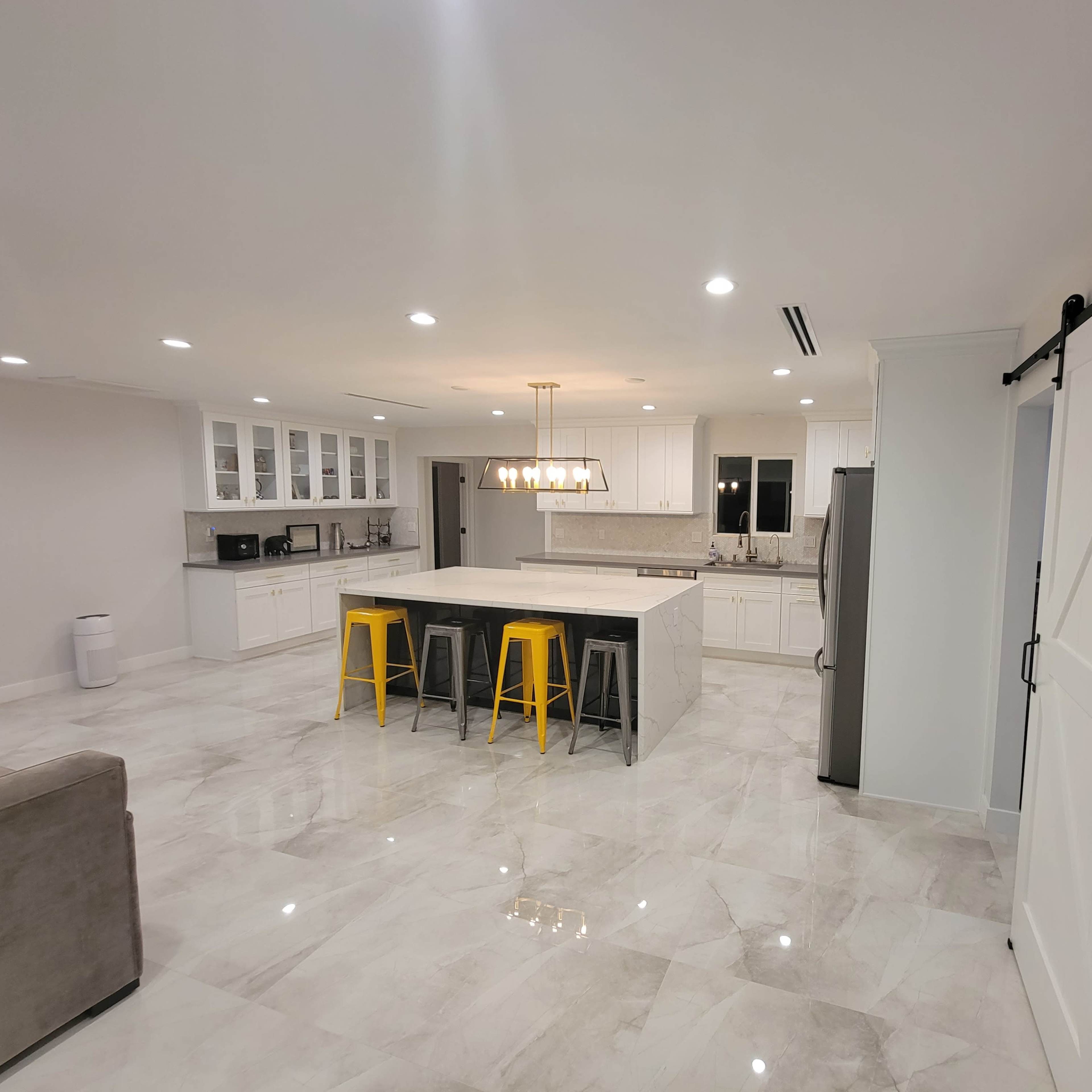 A modern kitchen with white cabinets, a large island with three stools, and a sliding barn door.