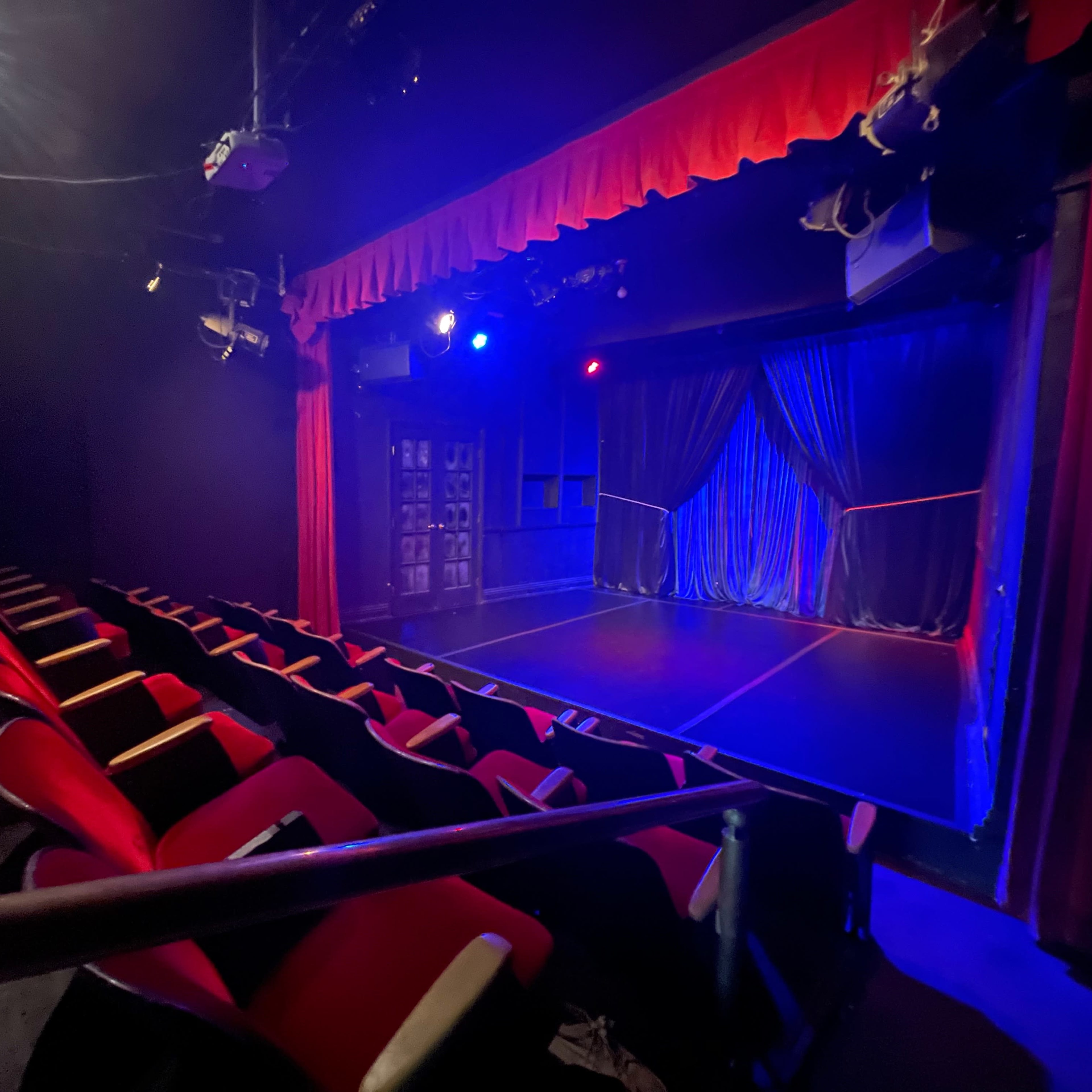 A small theater with red seating facing a stage illuminated by blue and purple lights.