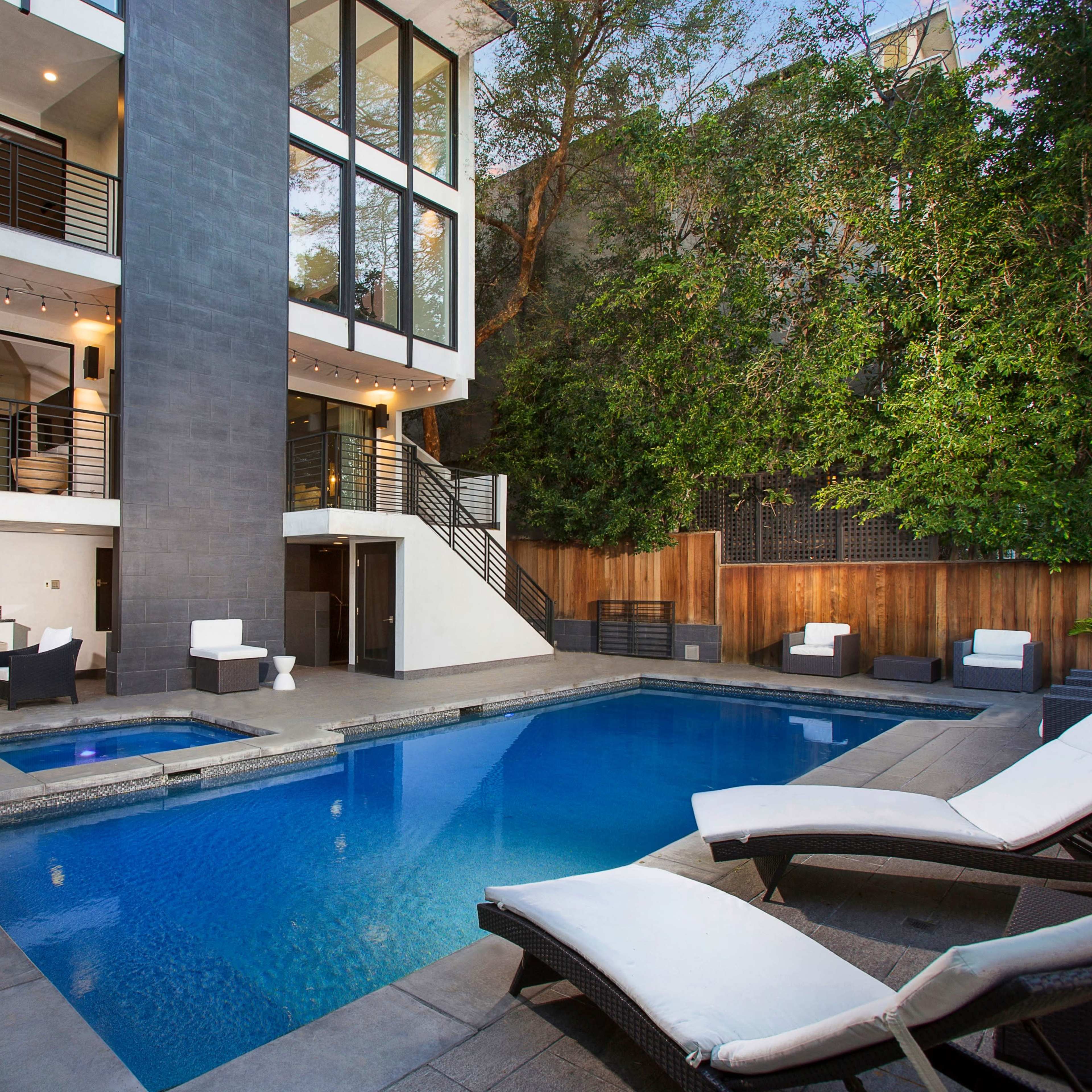 A modern home with large glass windows overlooking a swimming pool and outdoor seating area.