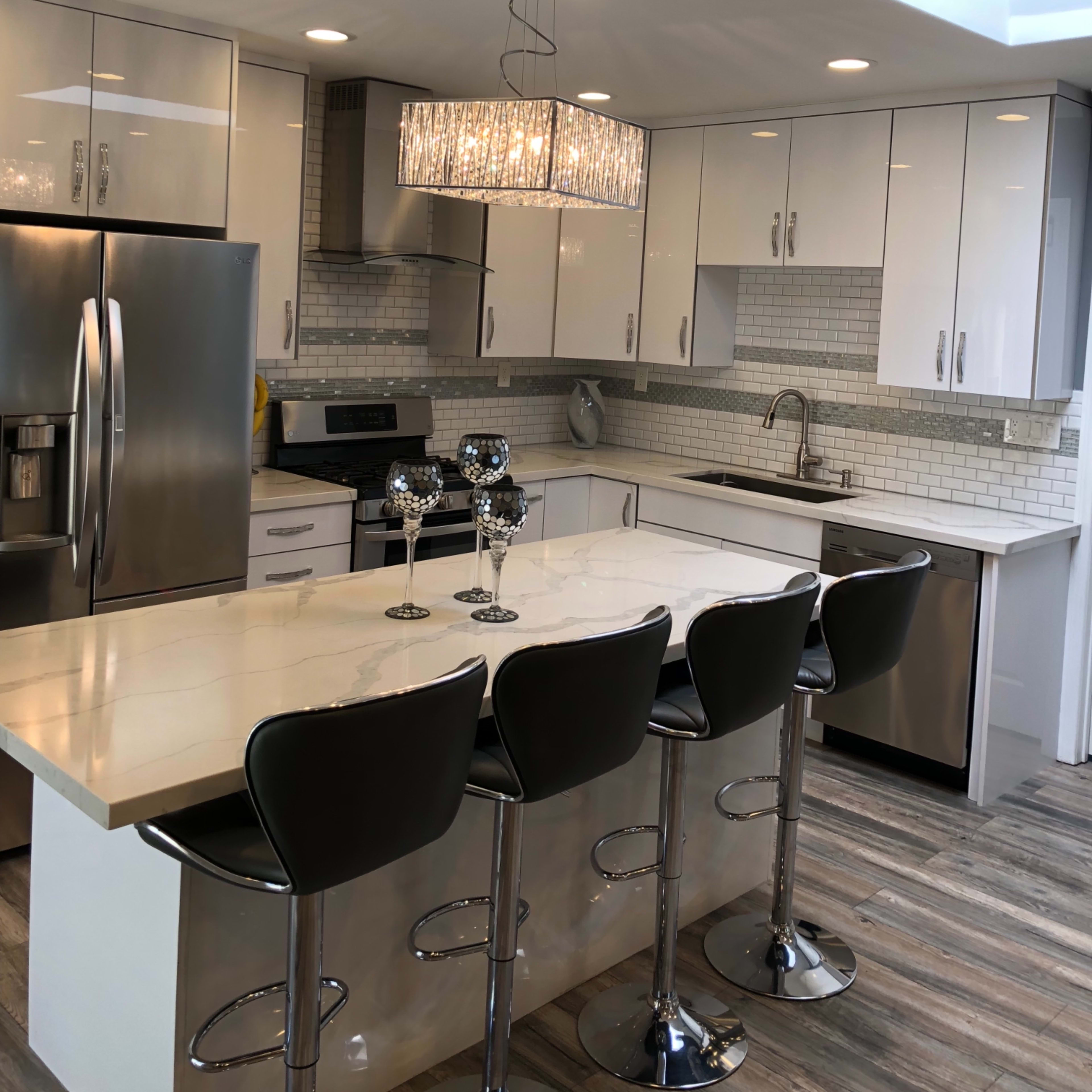 A modern kitchen with stainless steel appliances, white cabinetry, and a large island with four black barstools.