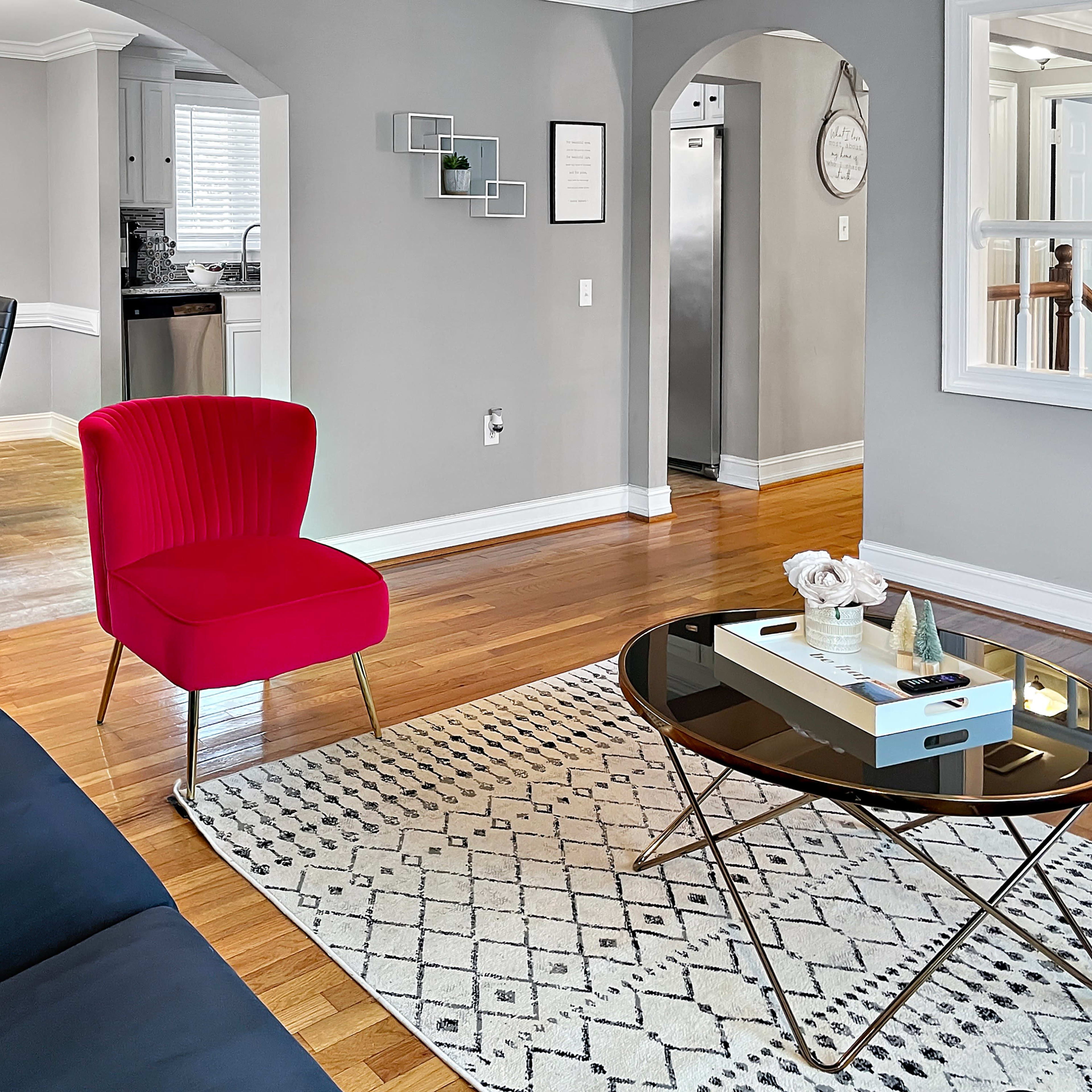 A modern living room with a navy sofa, a pink accent chair, a round coffee table, and a dining area in the background, featuring a black dining set.