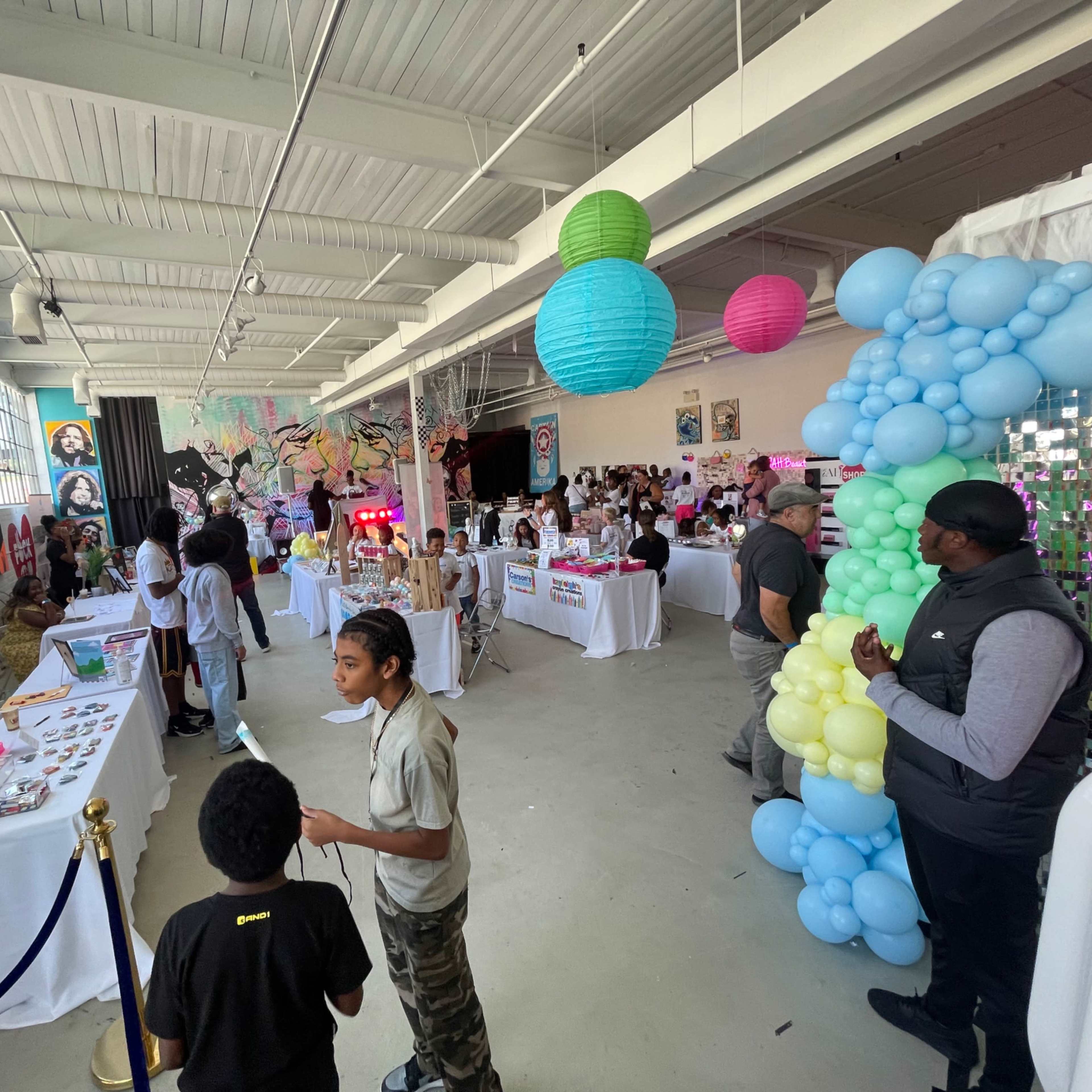 A lively indoor event space filled with booths and decorations, featuring families and children engaging in various activities.