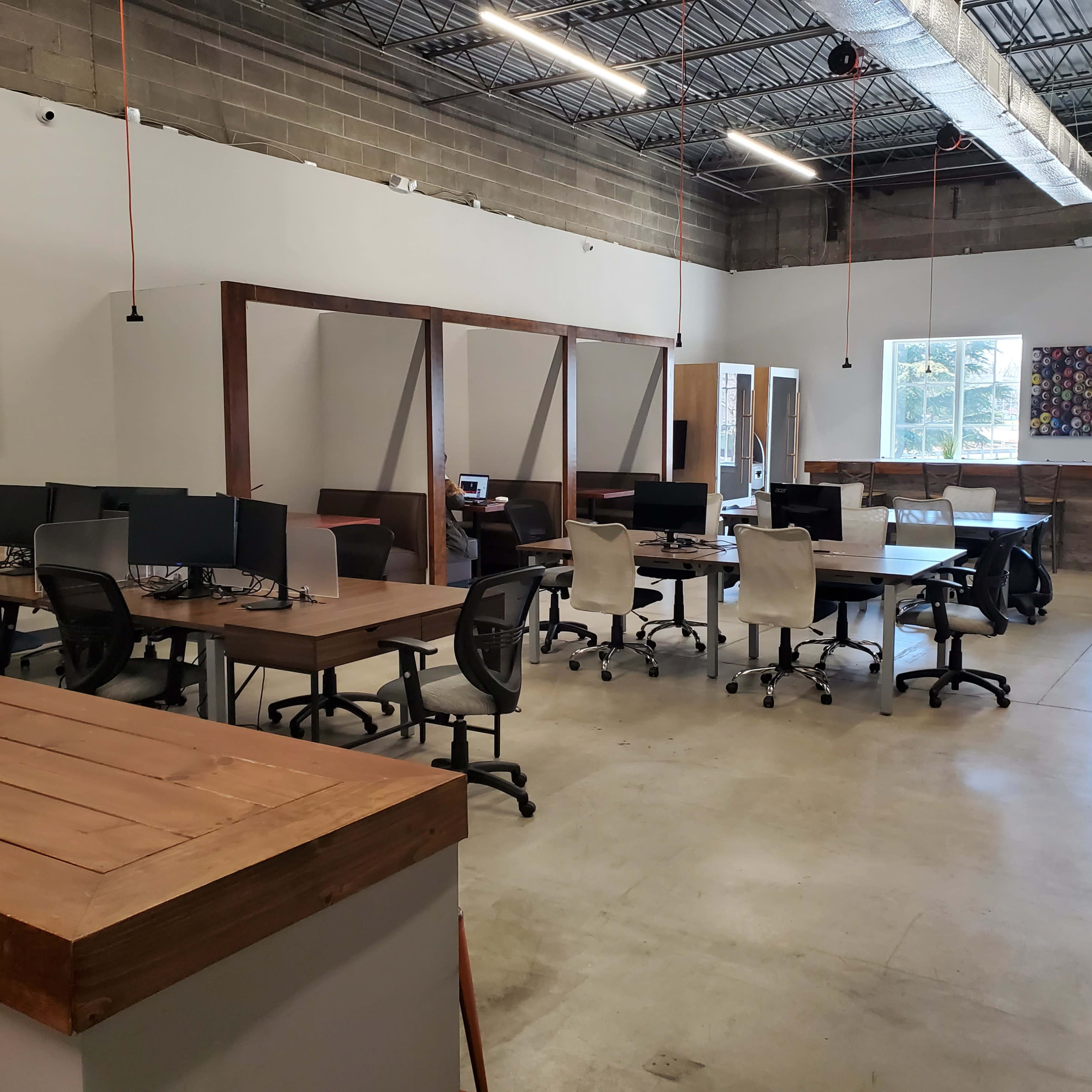 An open office space with multiple workstations, featuring wooden tables, chairs, and rows of computers.