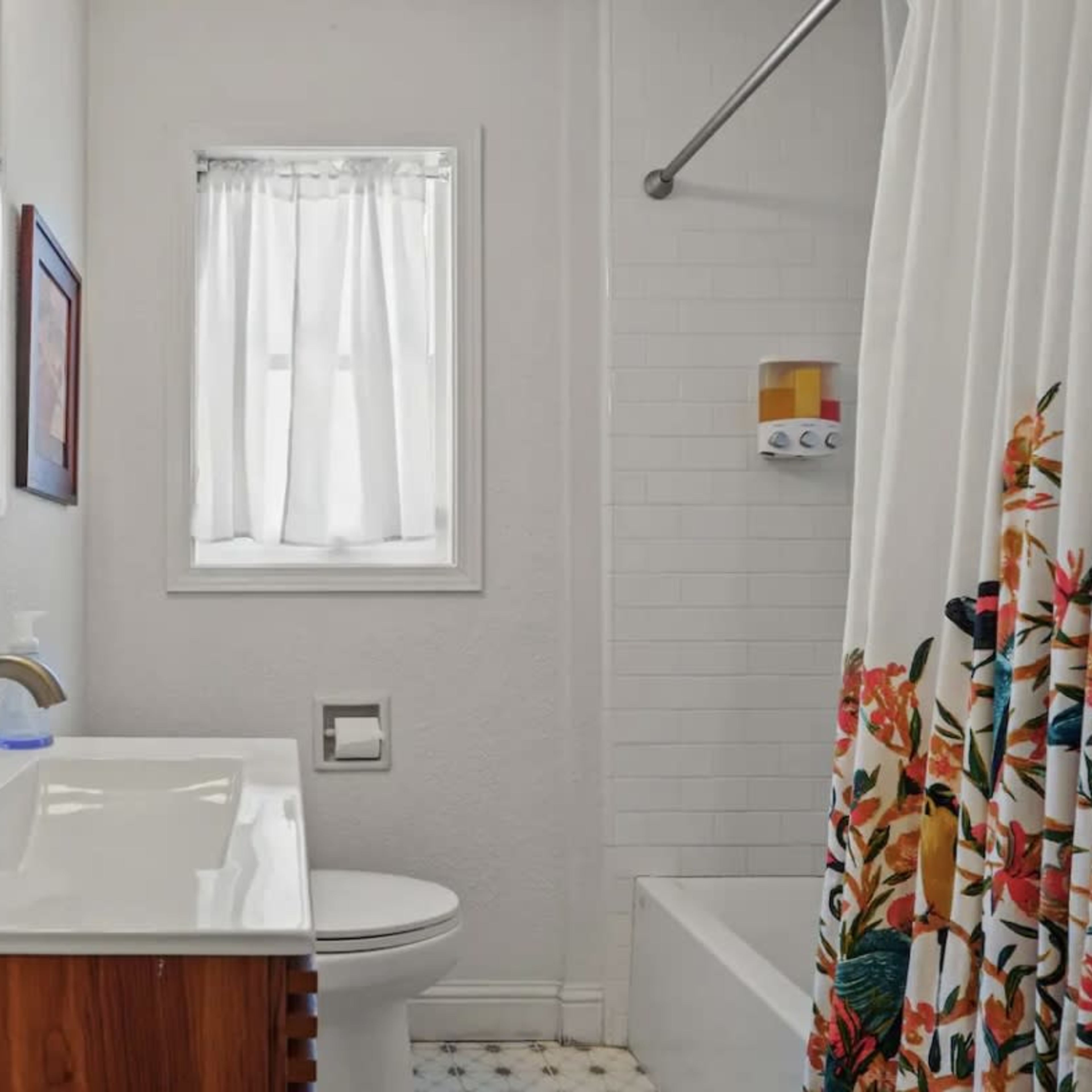 A compact bathroom featuring a sink with a wooden cabinet, a toilet, a bathtub, and a shower with a floral curtain.