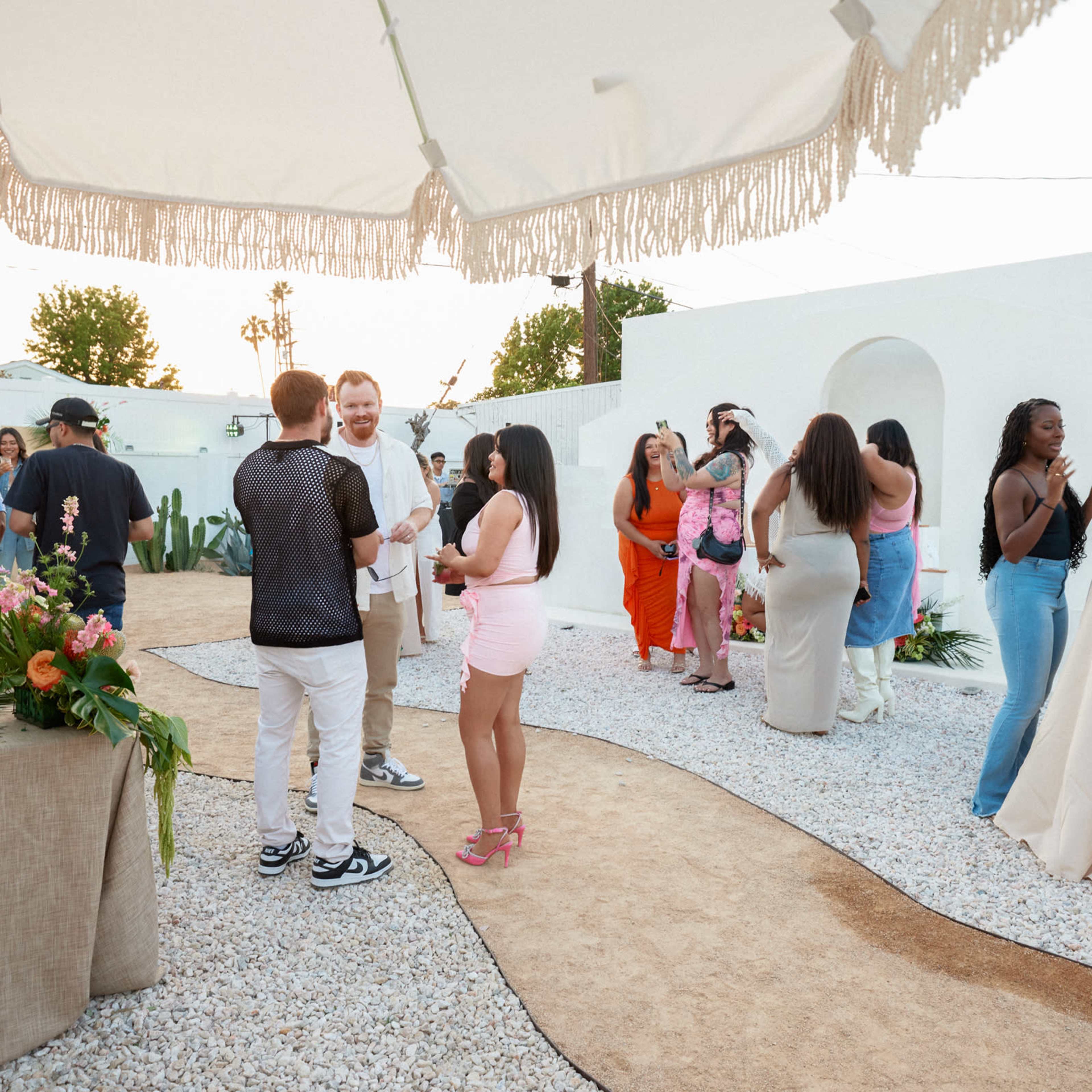 People socialize at an outdoor event in a garden setting with tables and decorations.