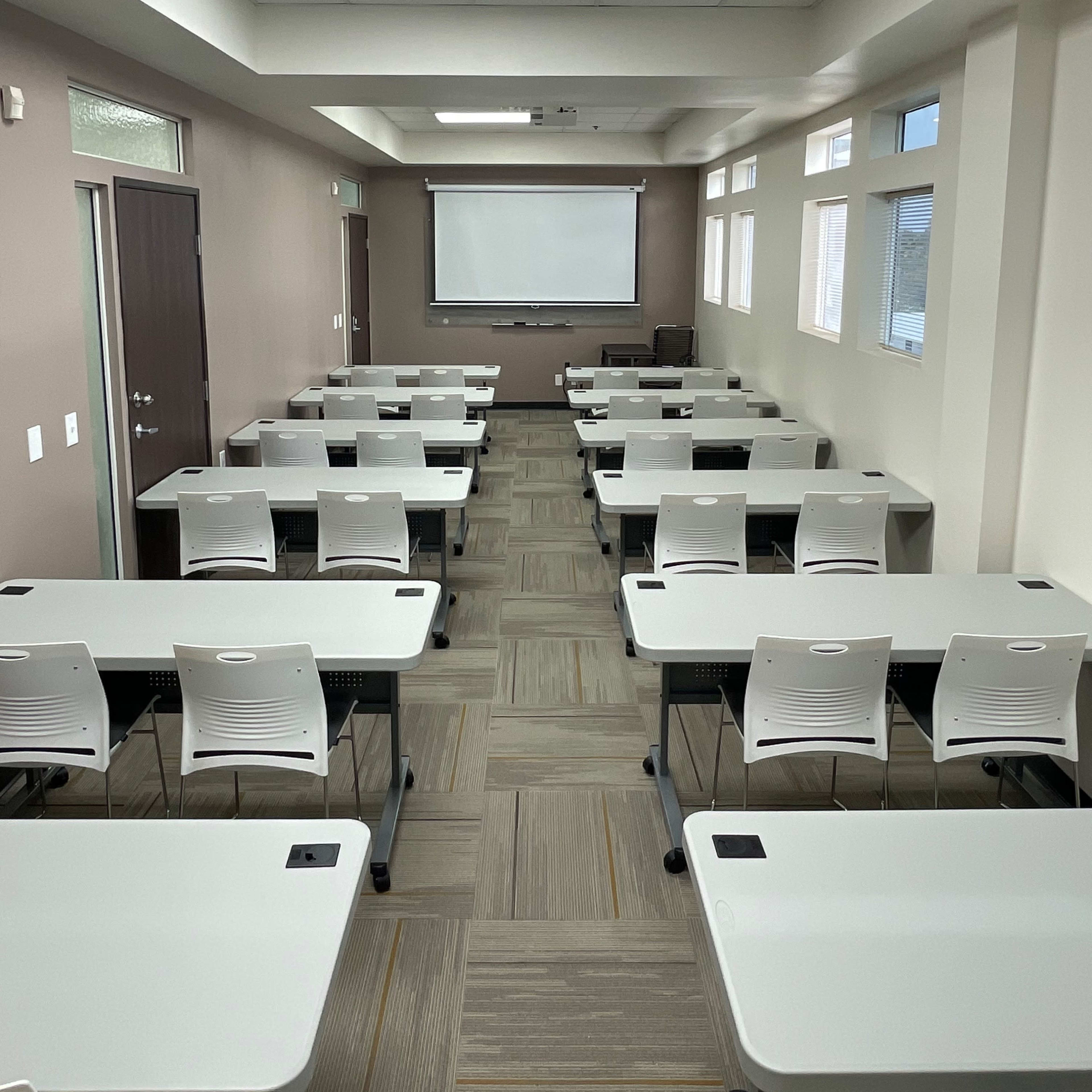 A well-organized classroom with multiple rows of desks and a projection screen at the front.