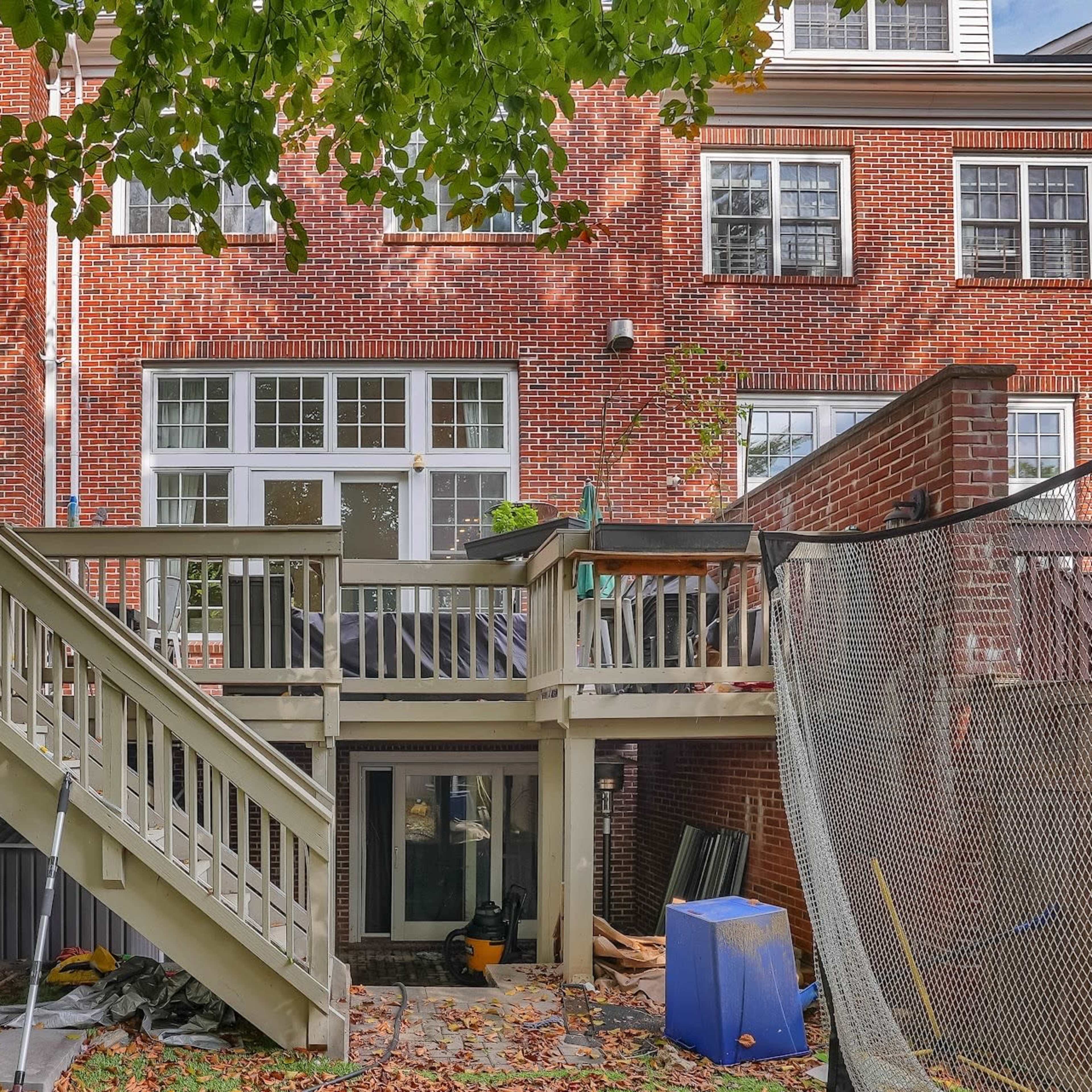The back of a brick house with a multi-level deck, climbing wall, and a netted area in the yard.