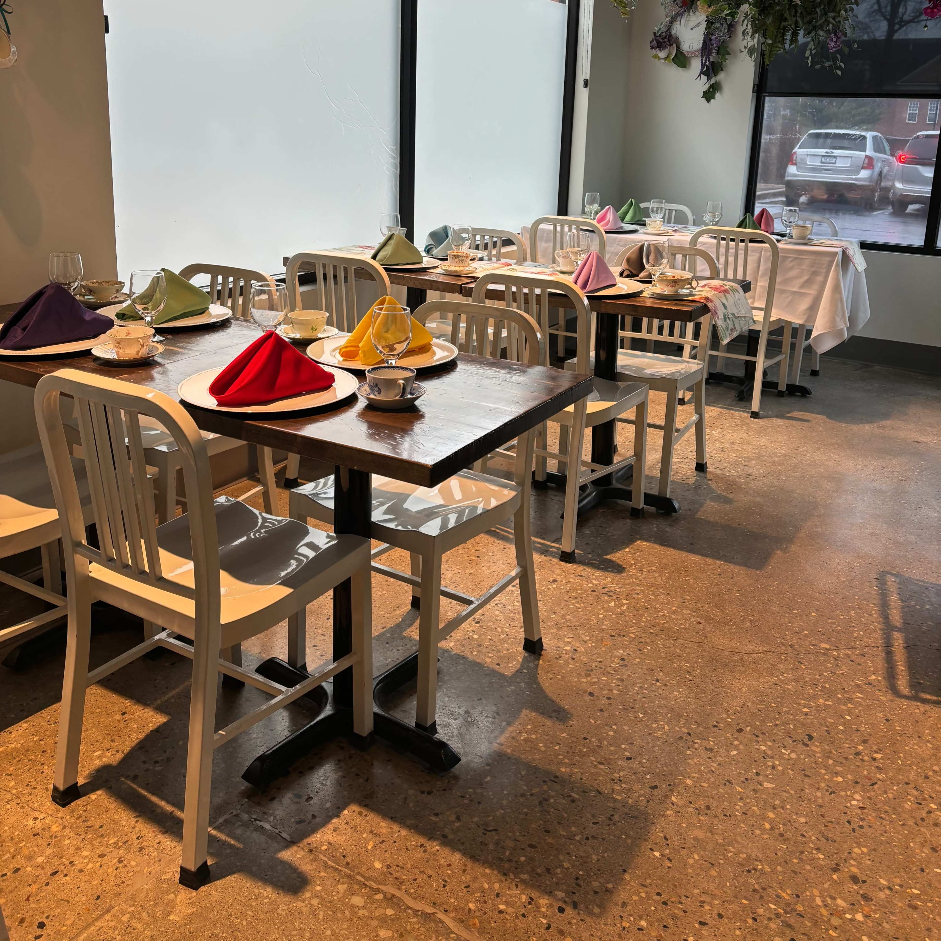 A dining area with white tables and chairs, each set with colored napkins, and adorned with hanging plants.