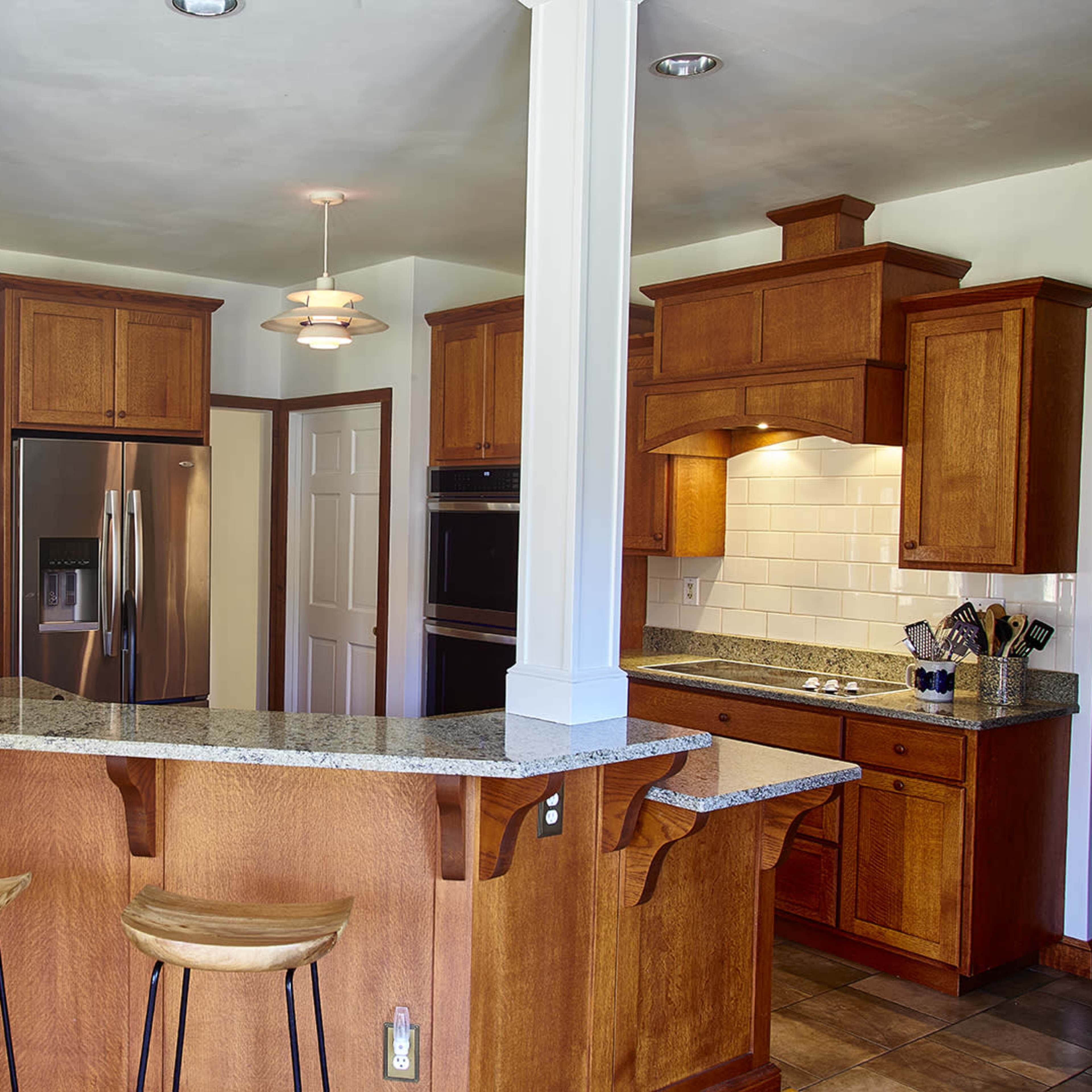A modern kitchen with wooden cabinetry, a granite countertop, and bar seating.