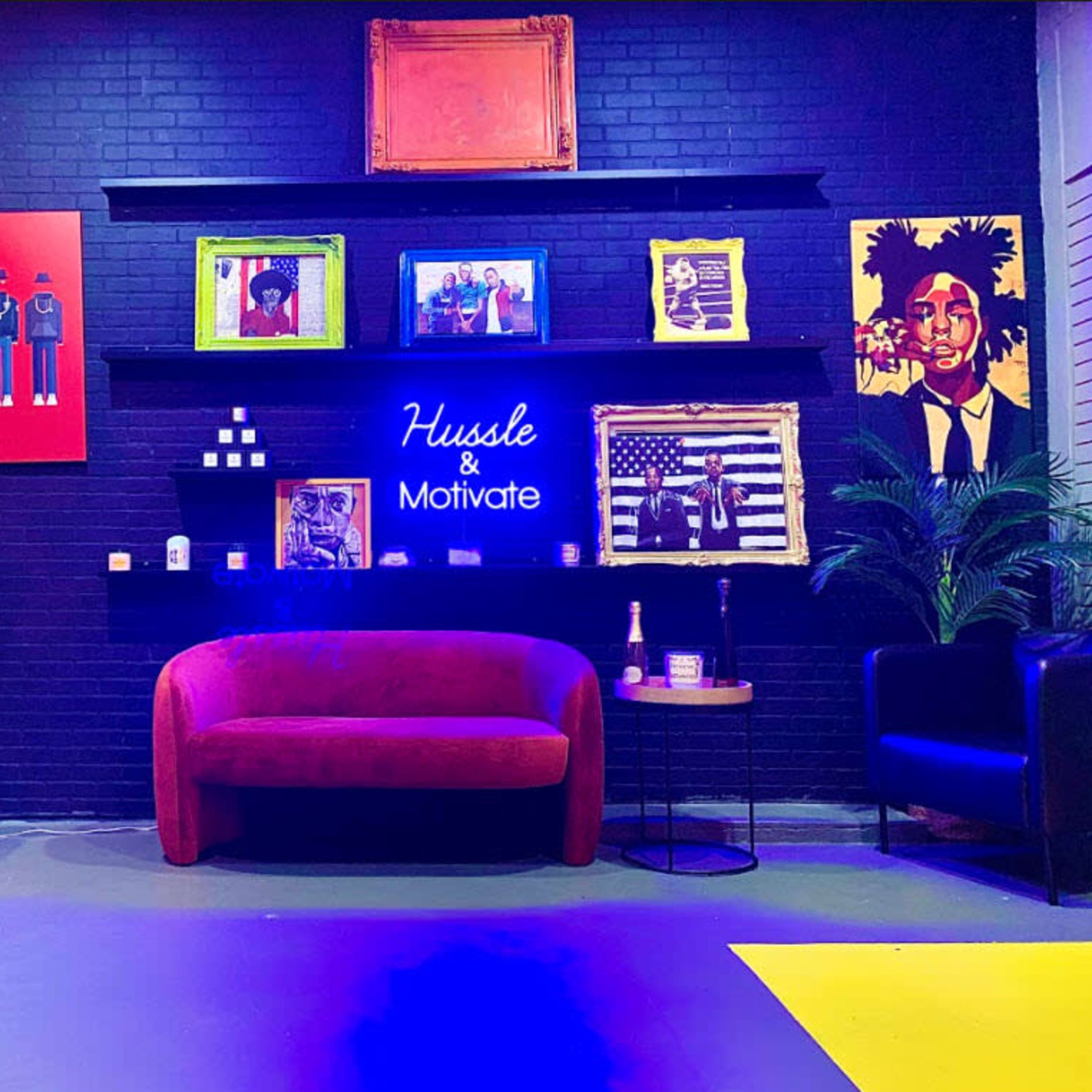 The scene features a modern lounge area with a red sofa, colorful artwork on the walls, and a neon sign that reads "Hustle & Motivate."