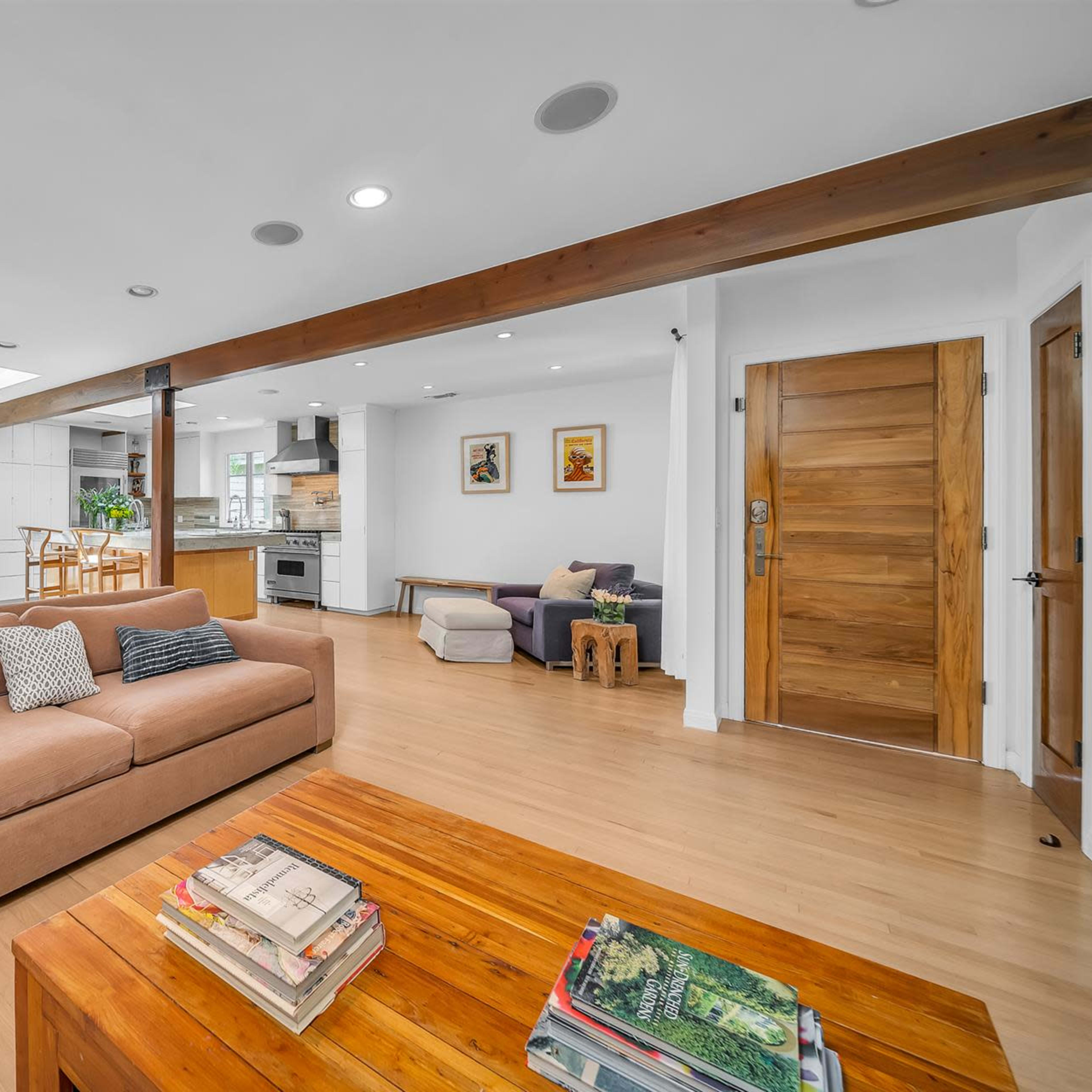 A modern, open living space featuring a sofa, wooden coffee table, and a dining area with large windows.