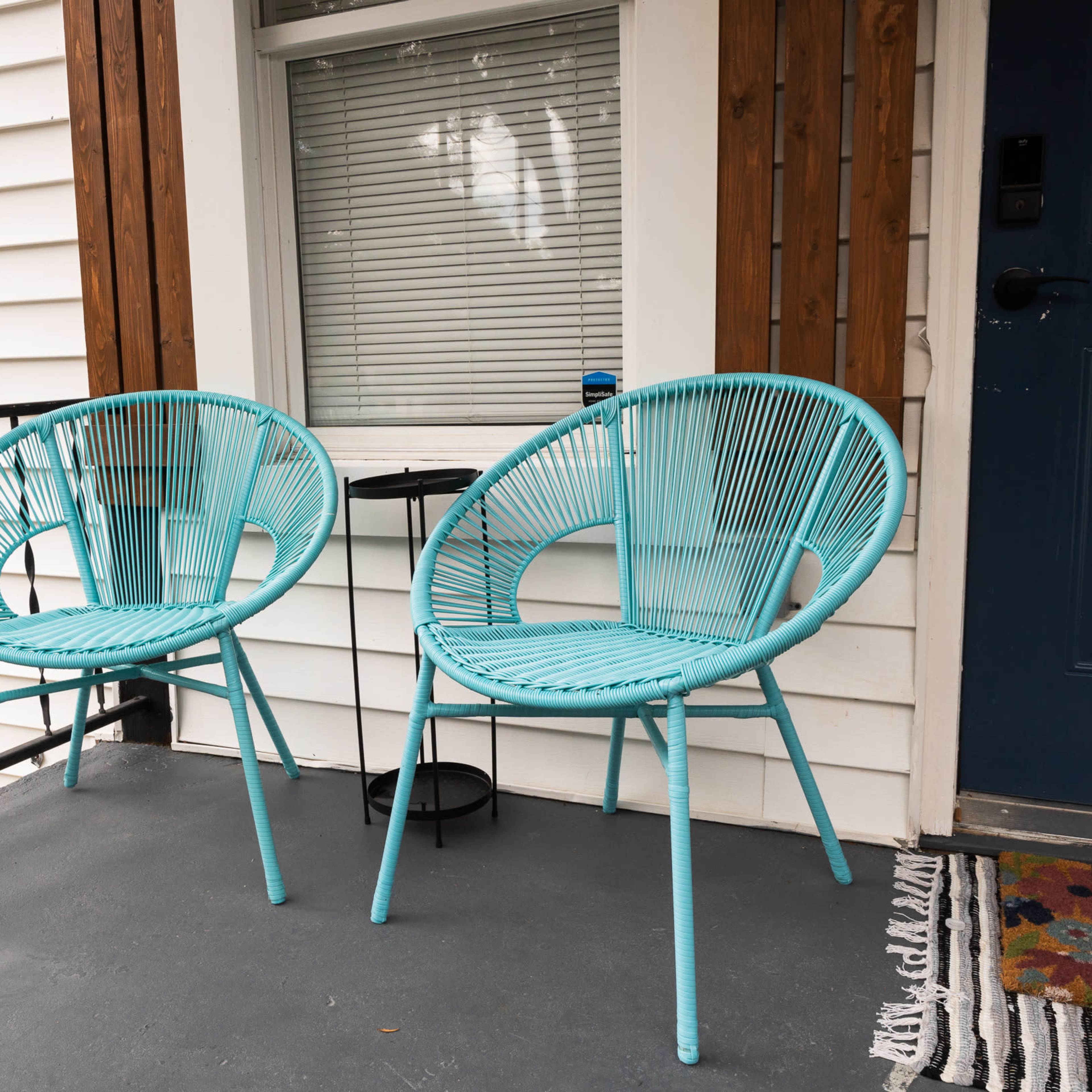 Two turquoise chairs are positioned on a porch next to a small round table, with a gray floor and white siding in the background.