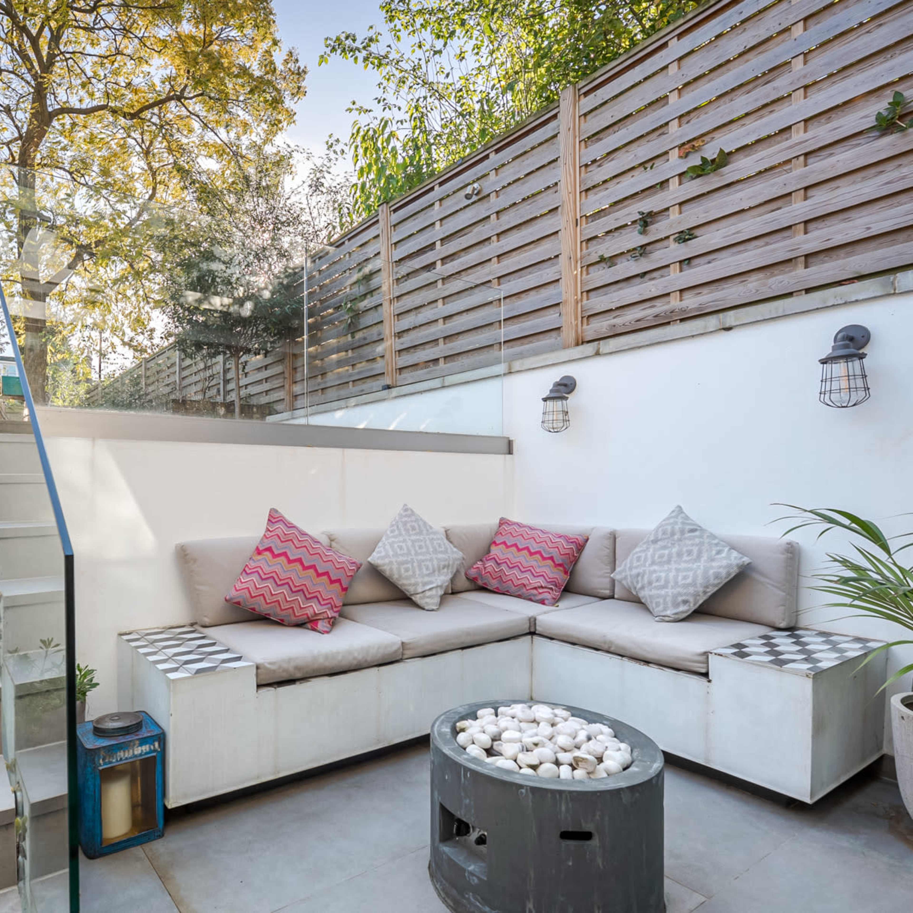 A modern outdoor seating area with a stairway, featuring a sectional sofa with decorative pillows, a coffee table, and plants.