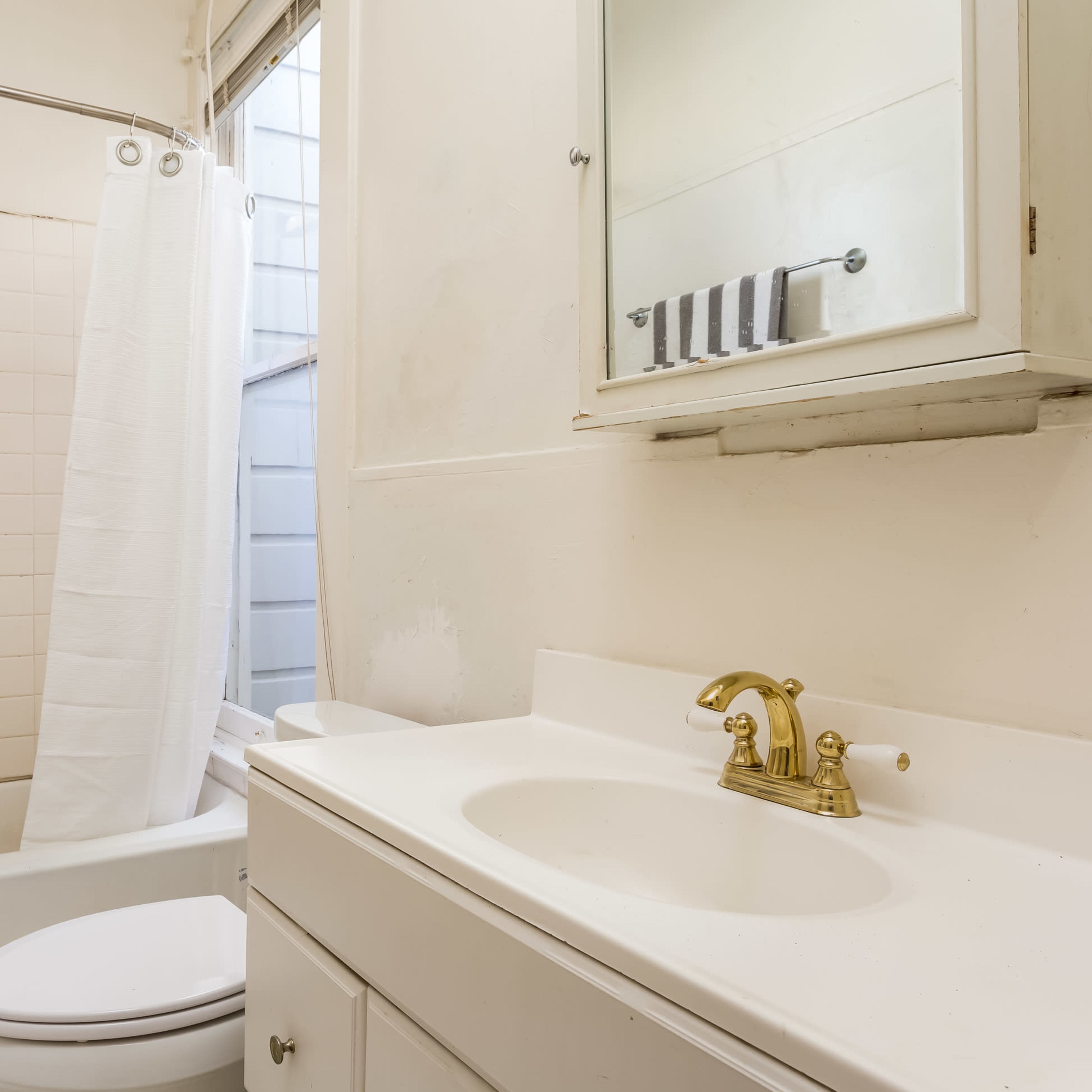 A small bathroom features a bathtub with a shower curtain, a toilet, and a sink with a mirror above it.