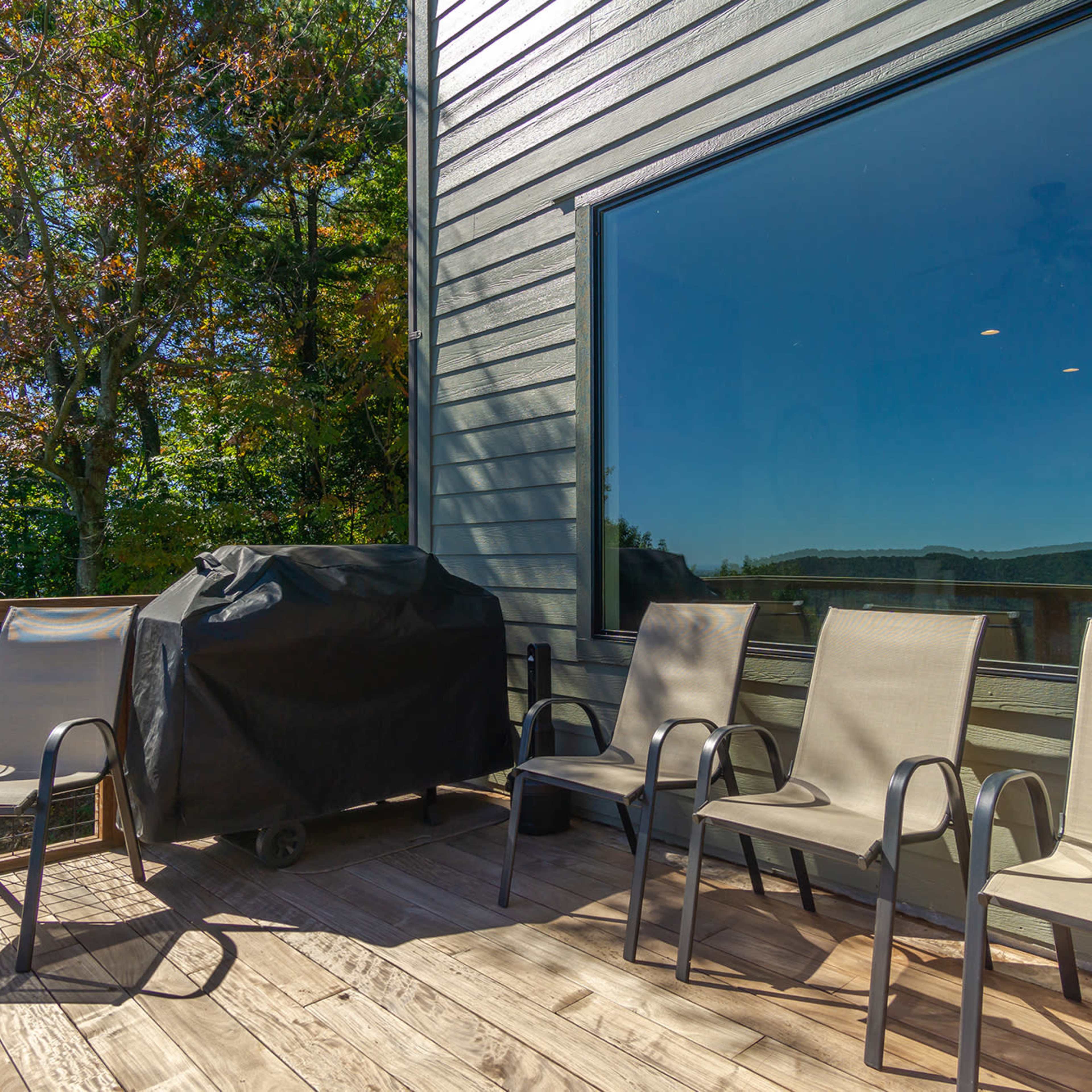 A deck features four chairs and a covered grill, with trees visible beyond a large window.