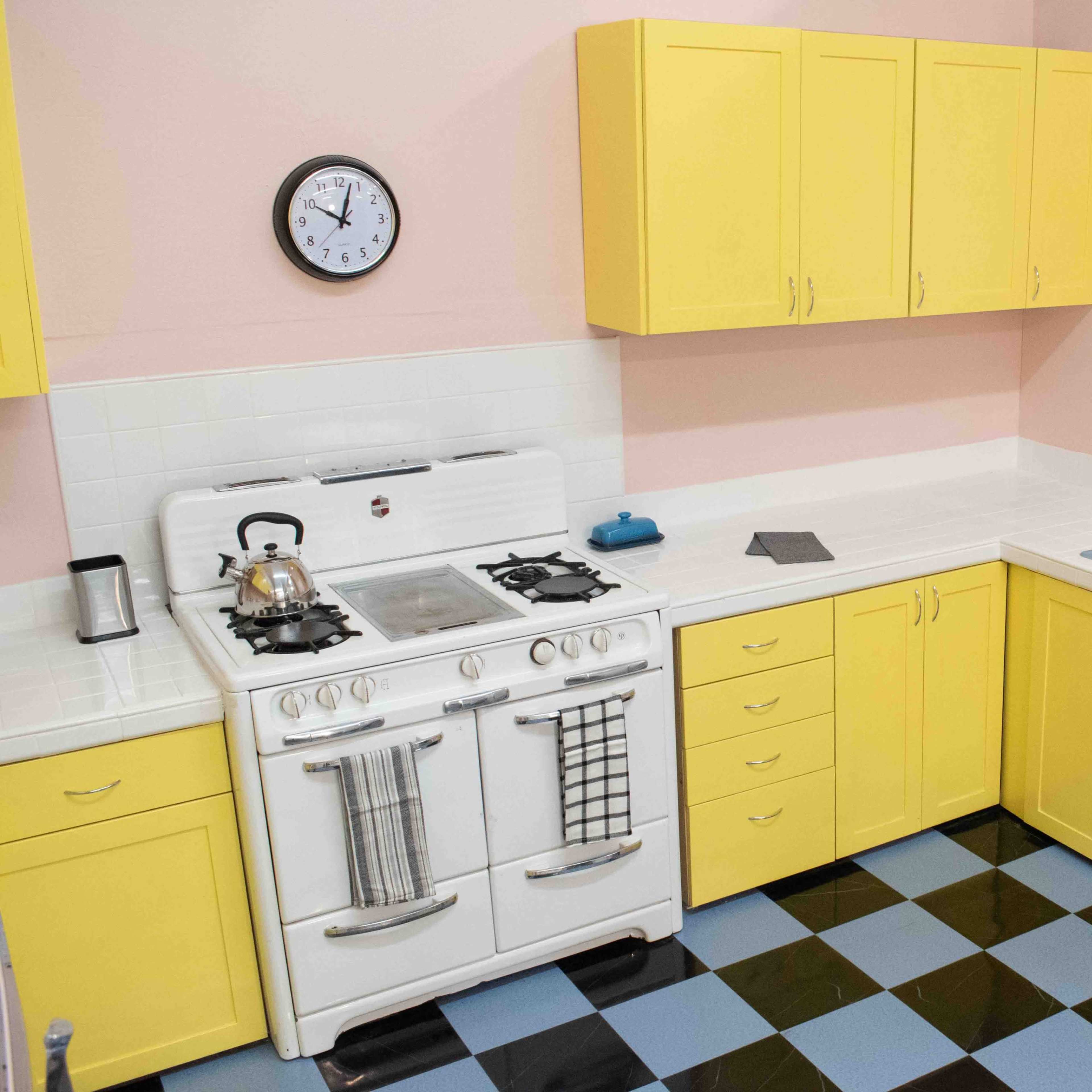 A kitchen with yellow cabinets, a white stove, a sink with a blue basin, and a checkered blue and black floor.