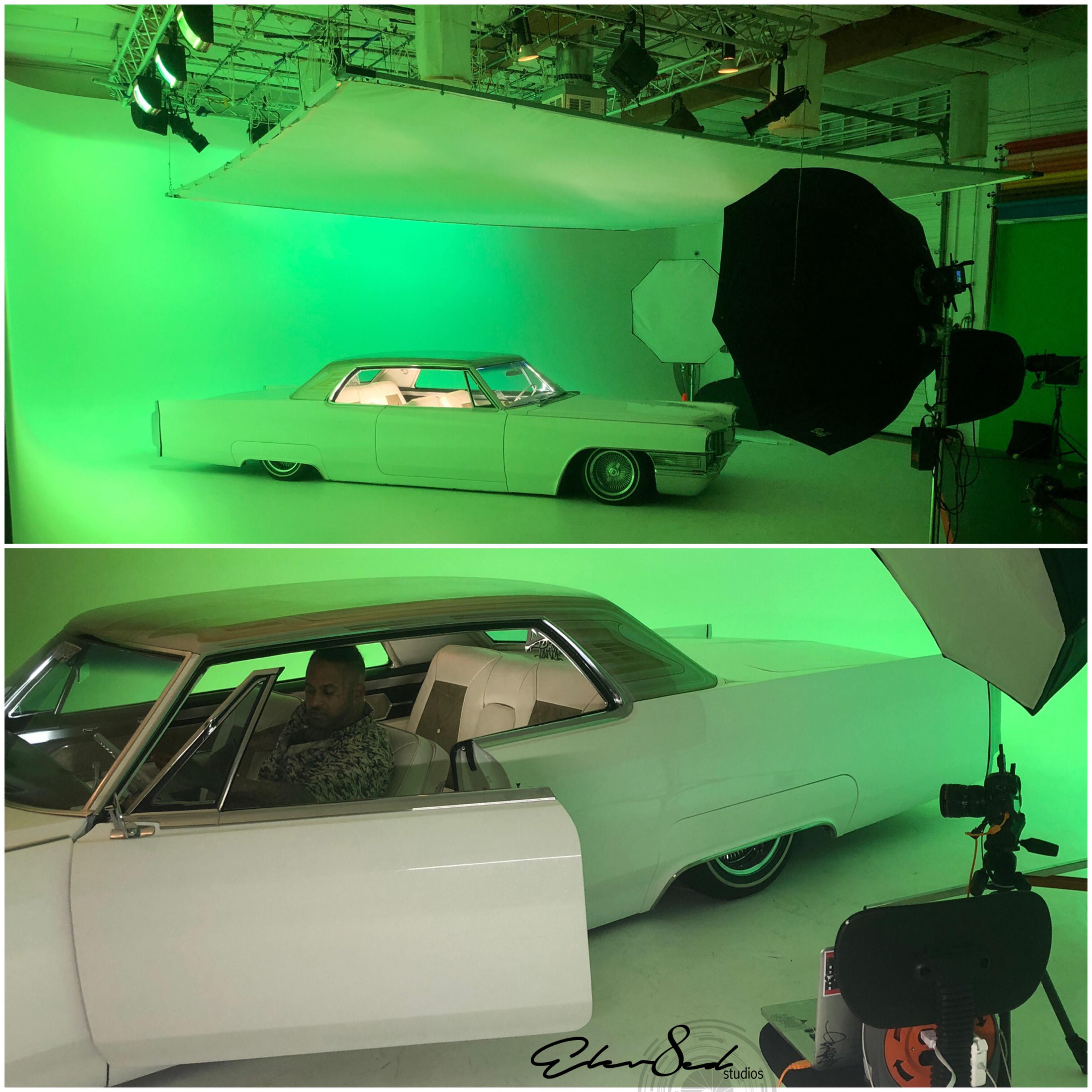 A vintage white car is positioned in a green studio with lighting equipment set up for photography.