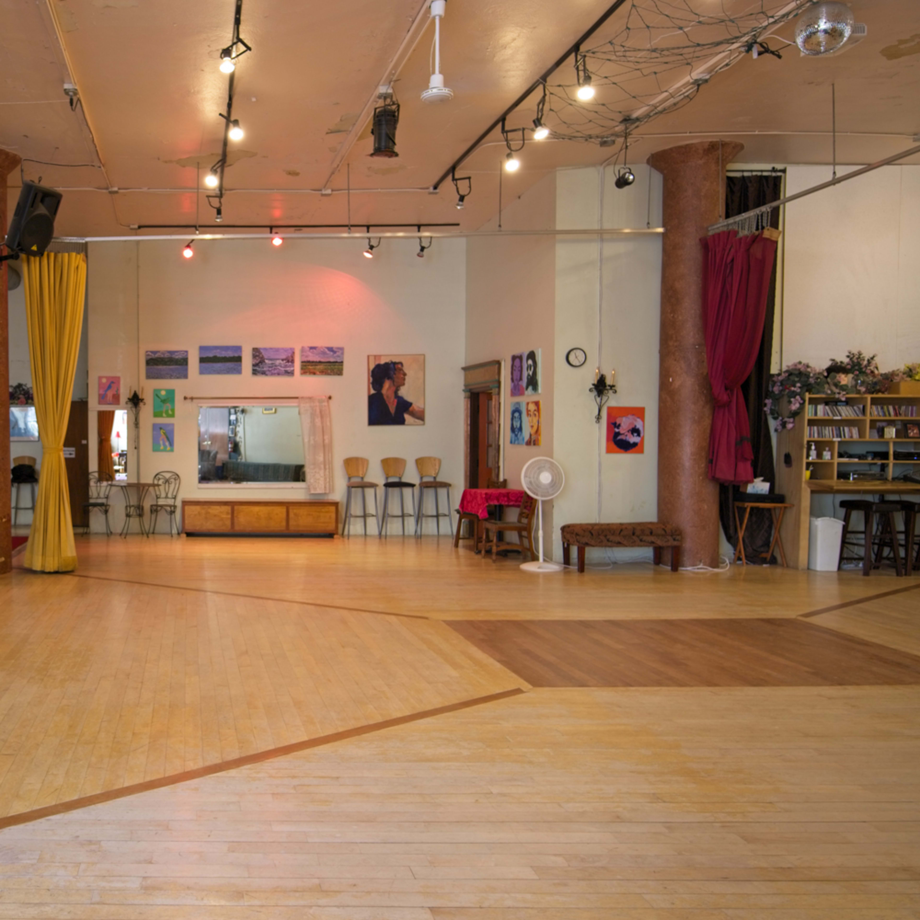 An interior space featuring wooden floors, colorful curtains, and a variety of artwork displayed on the walls.