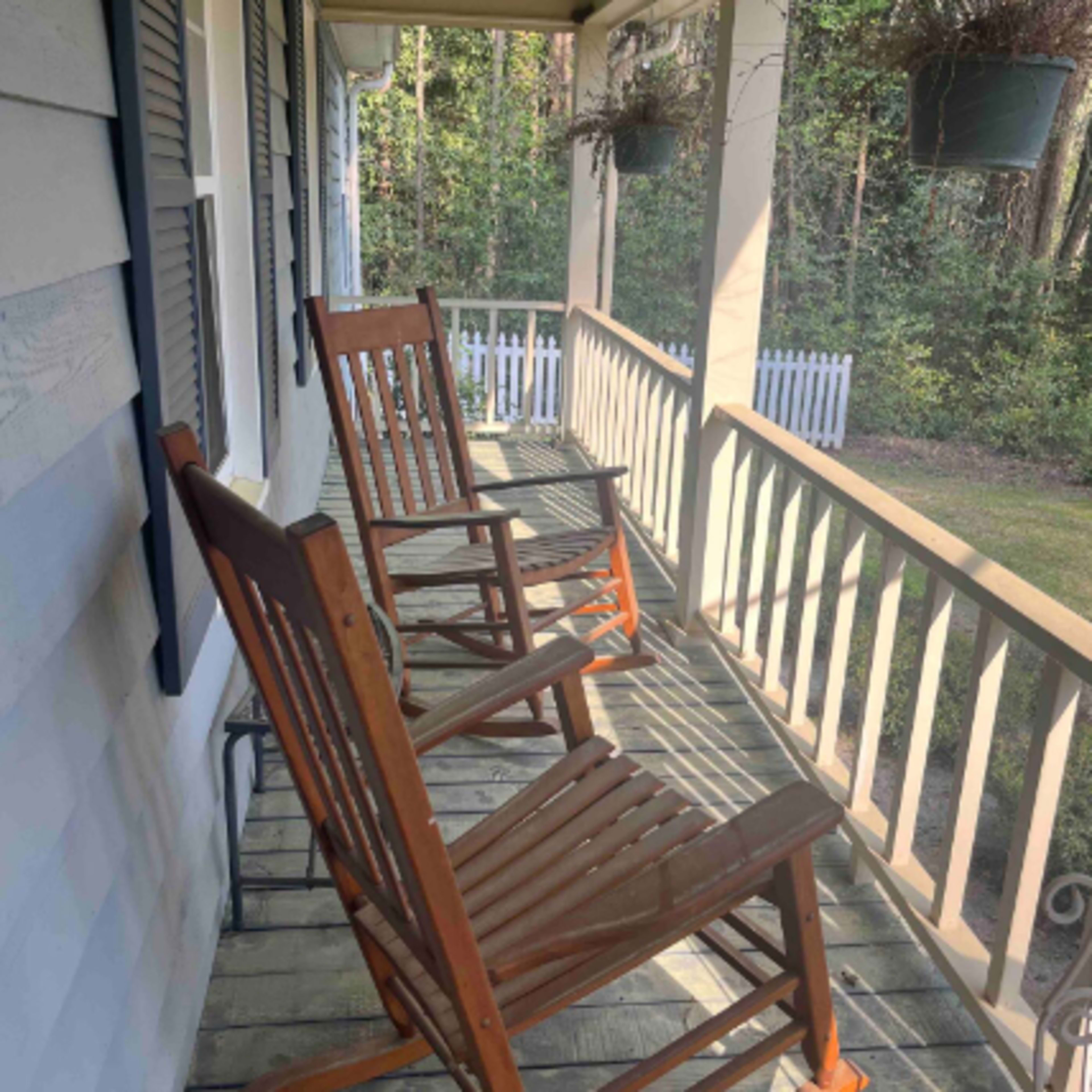 Two wooden rocking chairs on a porch, surrounded by trees and greenery.
