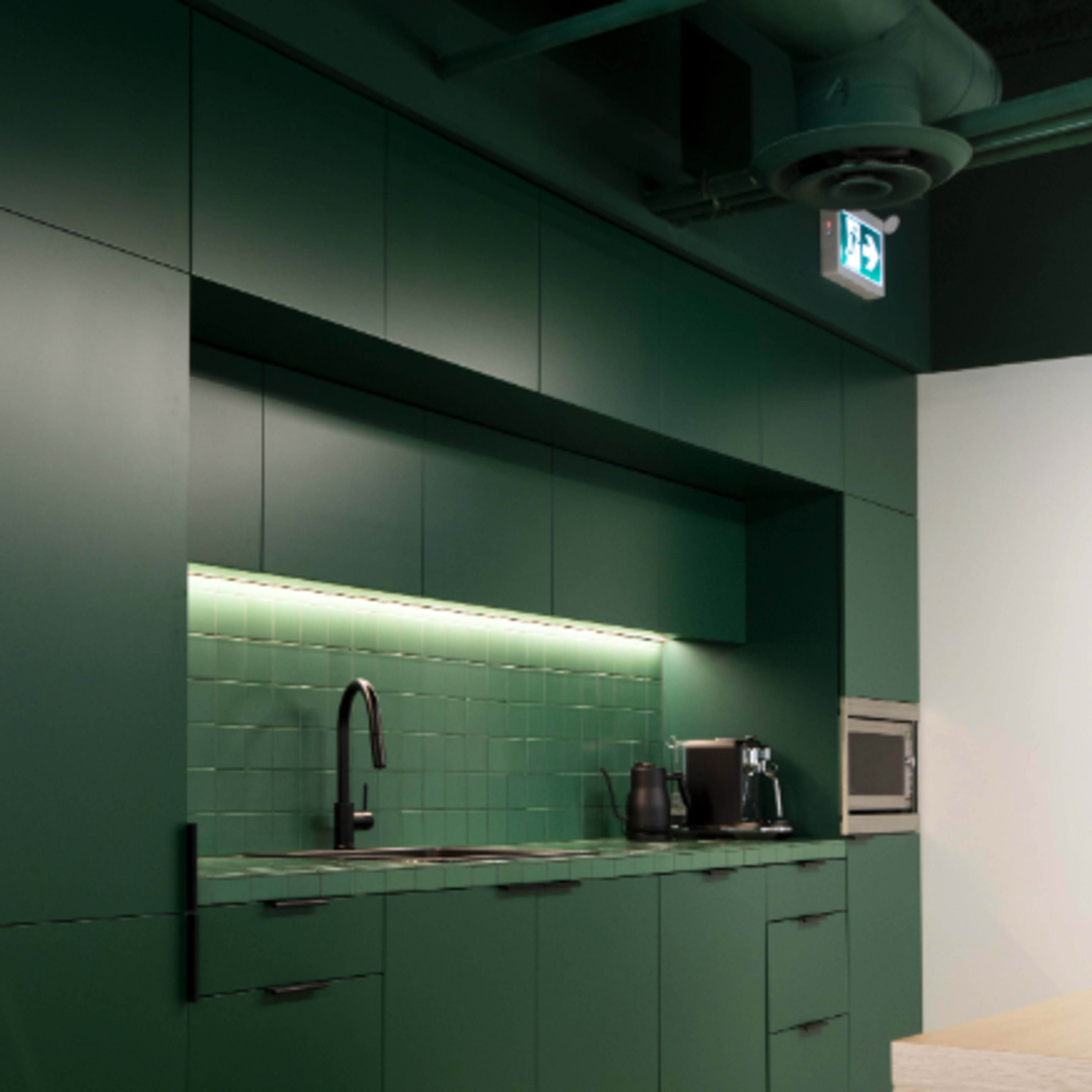 A modern kitchen with dark green cabinets, a backsplash of square tiles, and stainless steel appliances.