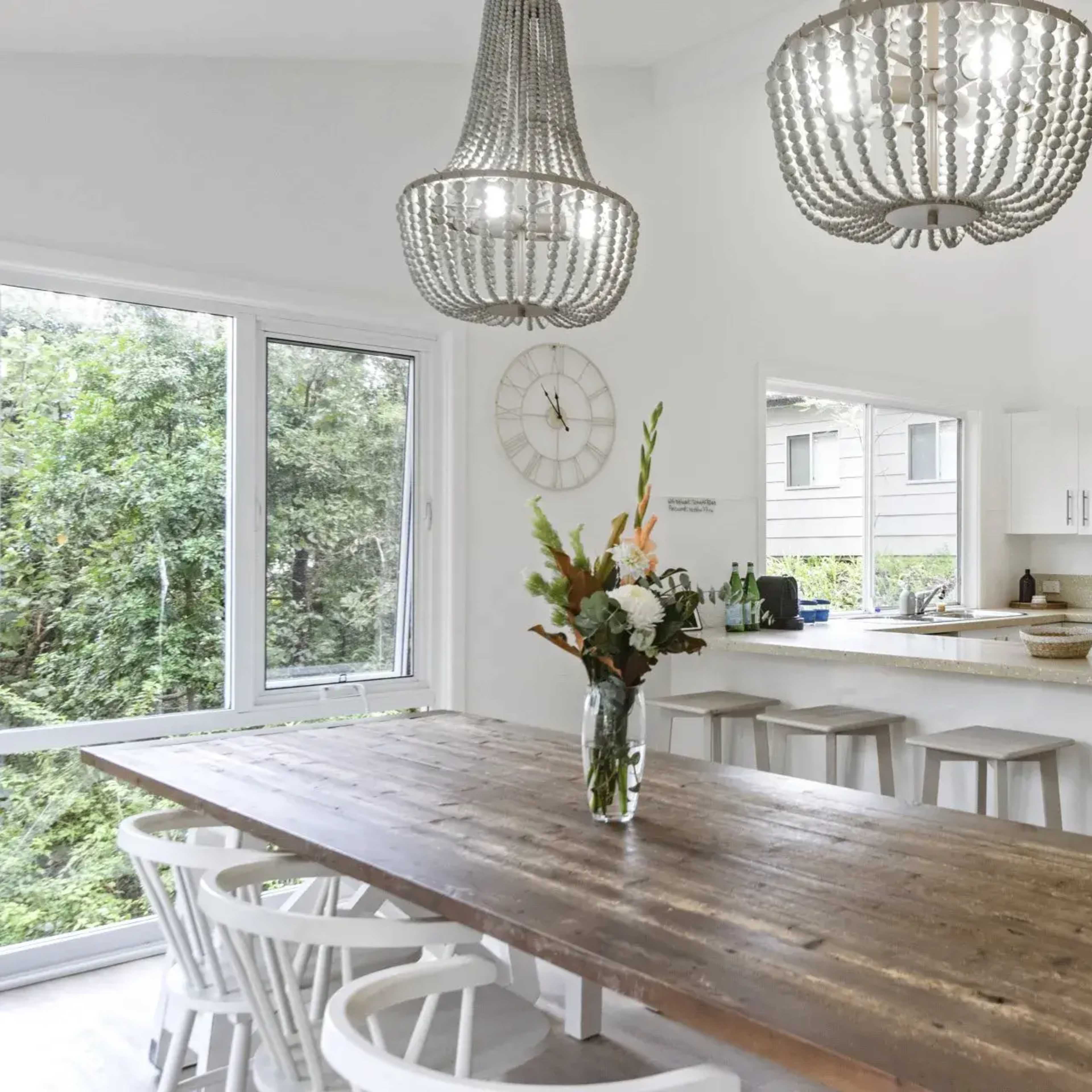 A modern kitchen with a large wooden dining table, white cabinetry, and three pendant lights hanging from the ceiling.