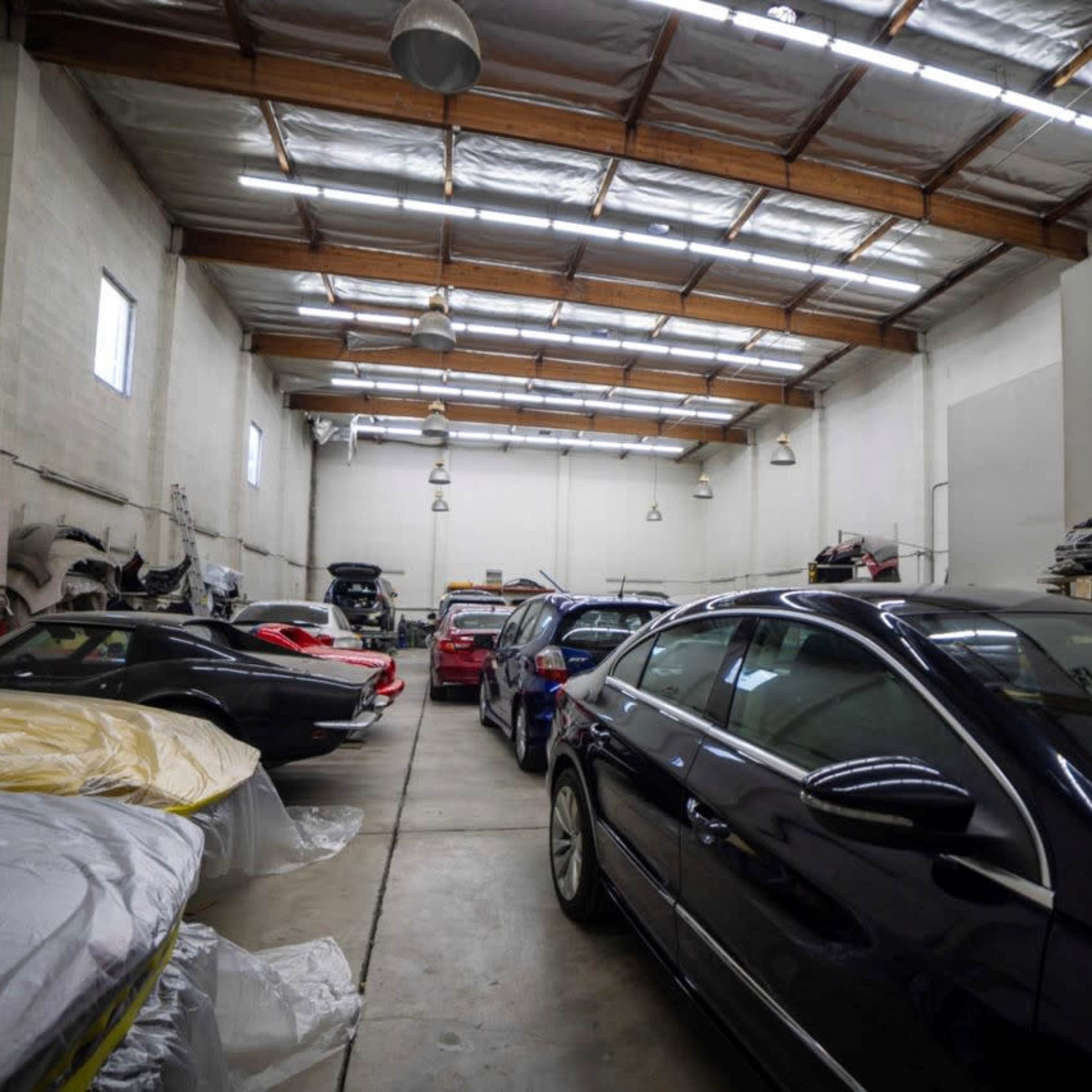 A spacious garage with several parked cars, some covered with protective sheets, and a high ceiling.